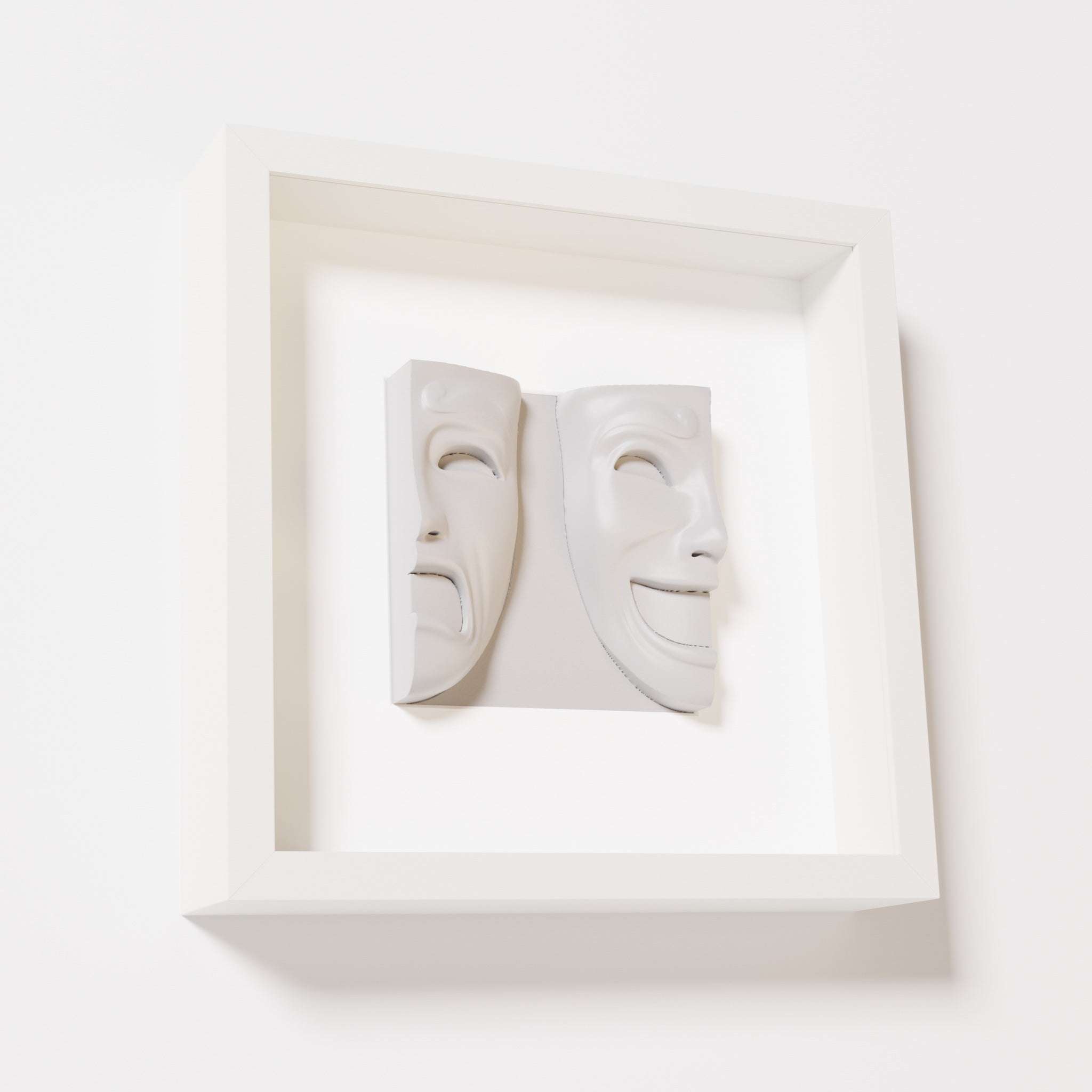 A close-up of a white shadowbox frame containing a marble white sculpture of 'Despair & Joy,' showcasing two expressive masks side by side: one with a sorrowful expression and the other with a joyful smile.