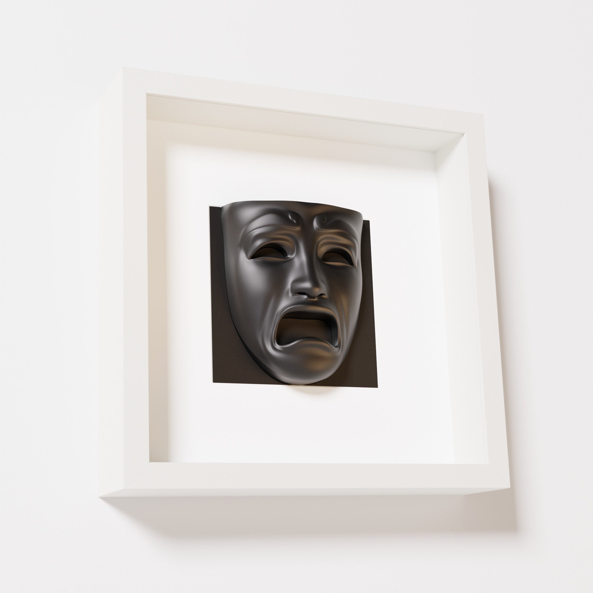 A close-up of a white shadowbox frame containing a matte black sculpture of 'Despair,' showcasing the expressive mask with furrowed brows, hollow eyes, and an open mouth.