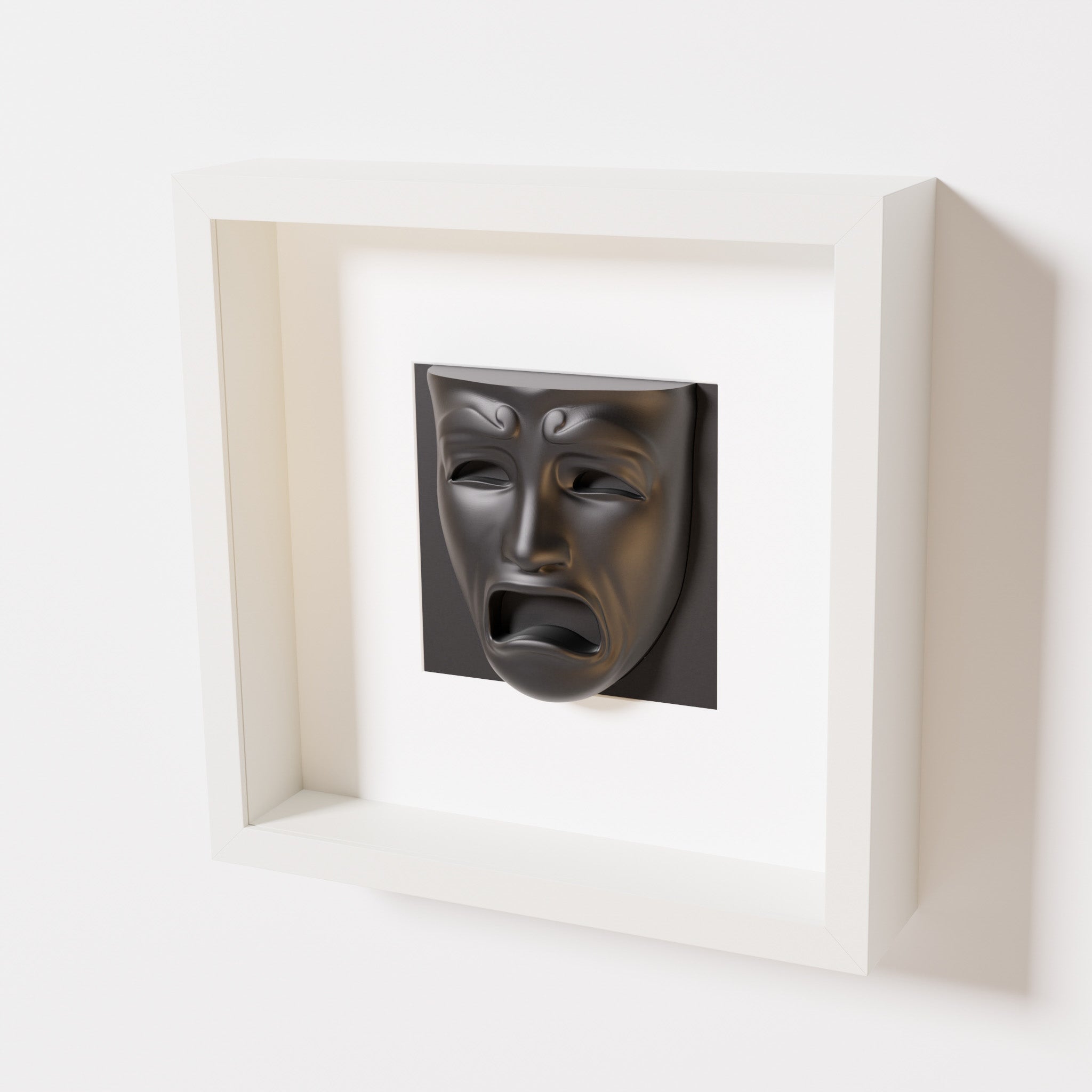 A close-up of a white shadowbox frame containing a matte black sculpture of 'Despair,' showcasing the expressive mask with furrowed brows, hollow eyes, and an open mouth.