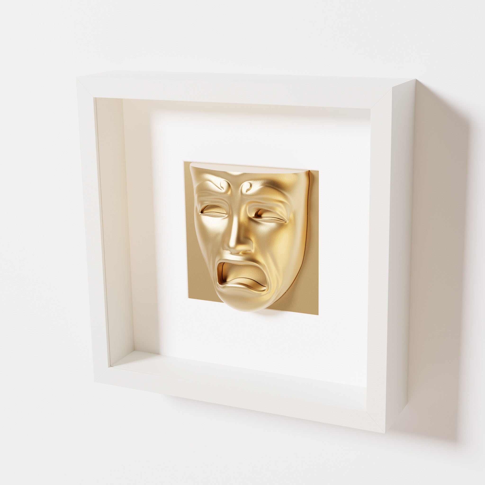 A close-up of a white shadowbox frame containing a chrome gold sculpture of 'Despair,' showcasing the expressive mask with furrowed brows, hollow eyes, and an open mouth.