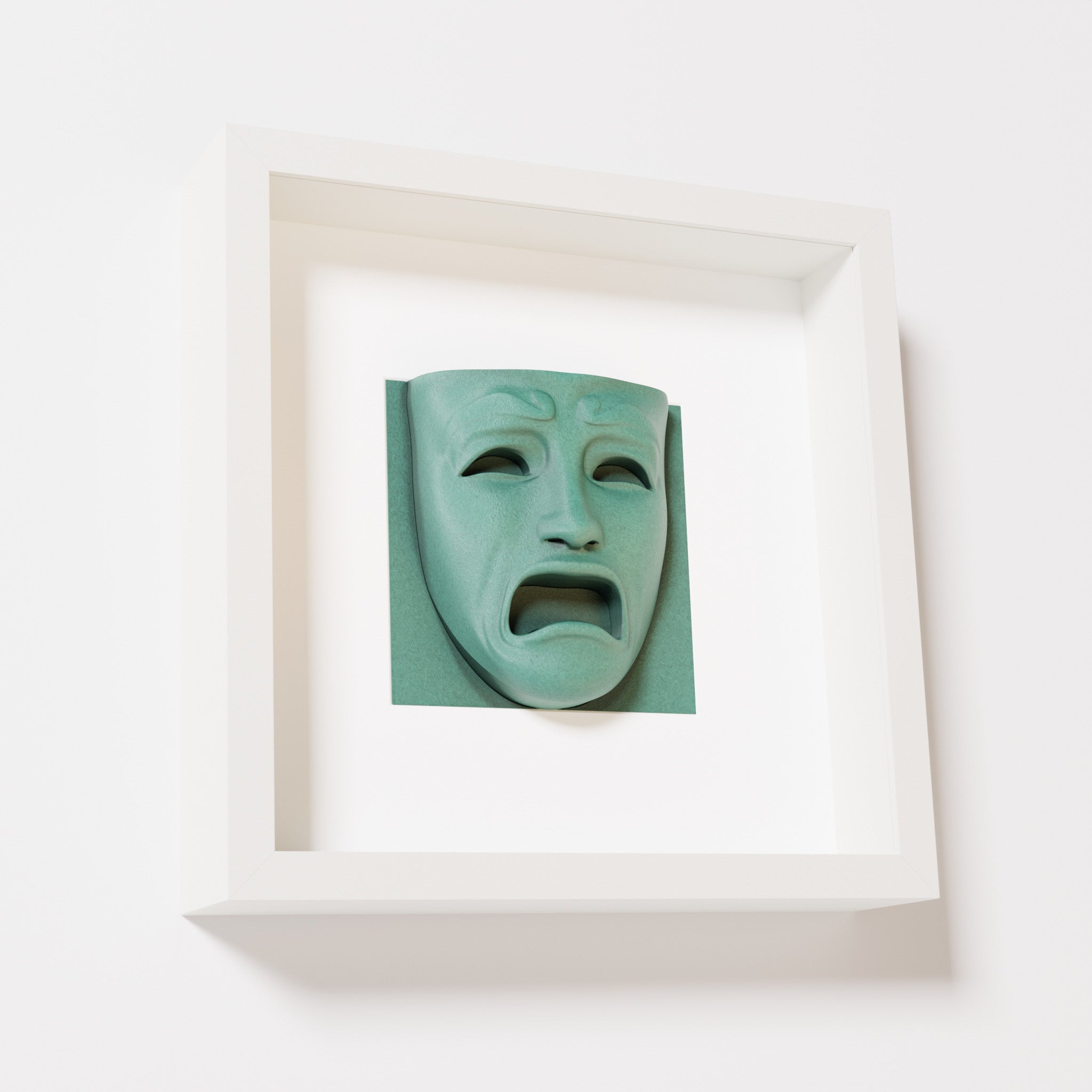 A close-up of a white shadowbox frame containing an old patina sculpture of 'Despair,' showcasing the expressive mask with furrowed brows, hollow eyes, and an open mouth.