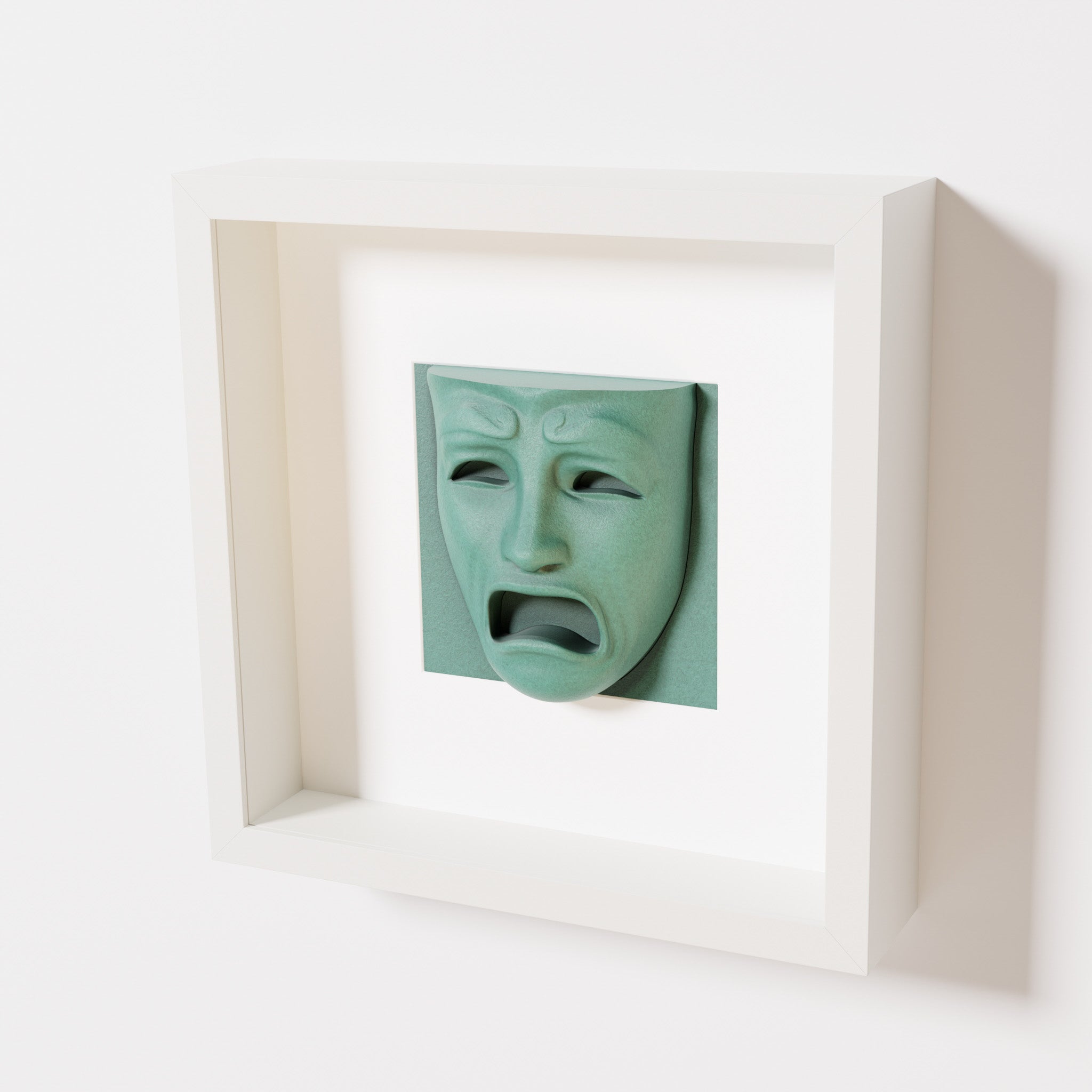 A close-up of a white shadowbox frame containing an old patina sculpture of 'Despair,' showcasing the expressive mask with furrowed brows, hollow eyes, and an open mouth.