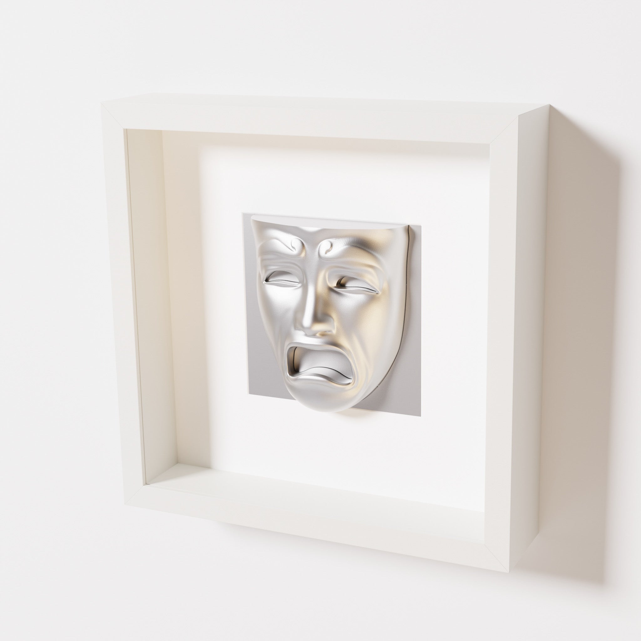 A close-up of a white shadowbox frame containing a chrome silver sculpture of 'Despair,' showcasing the expressive mask with furrowed brows, hollow eyes, and an open mouth.