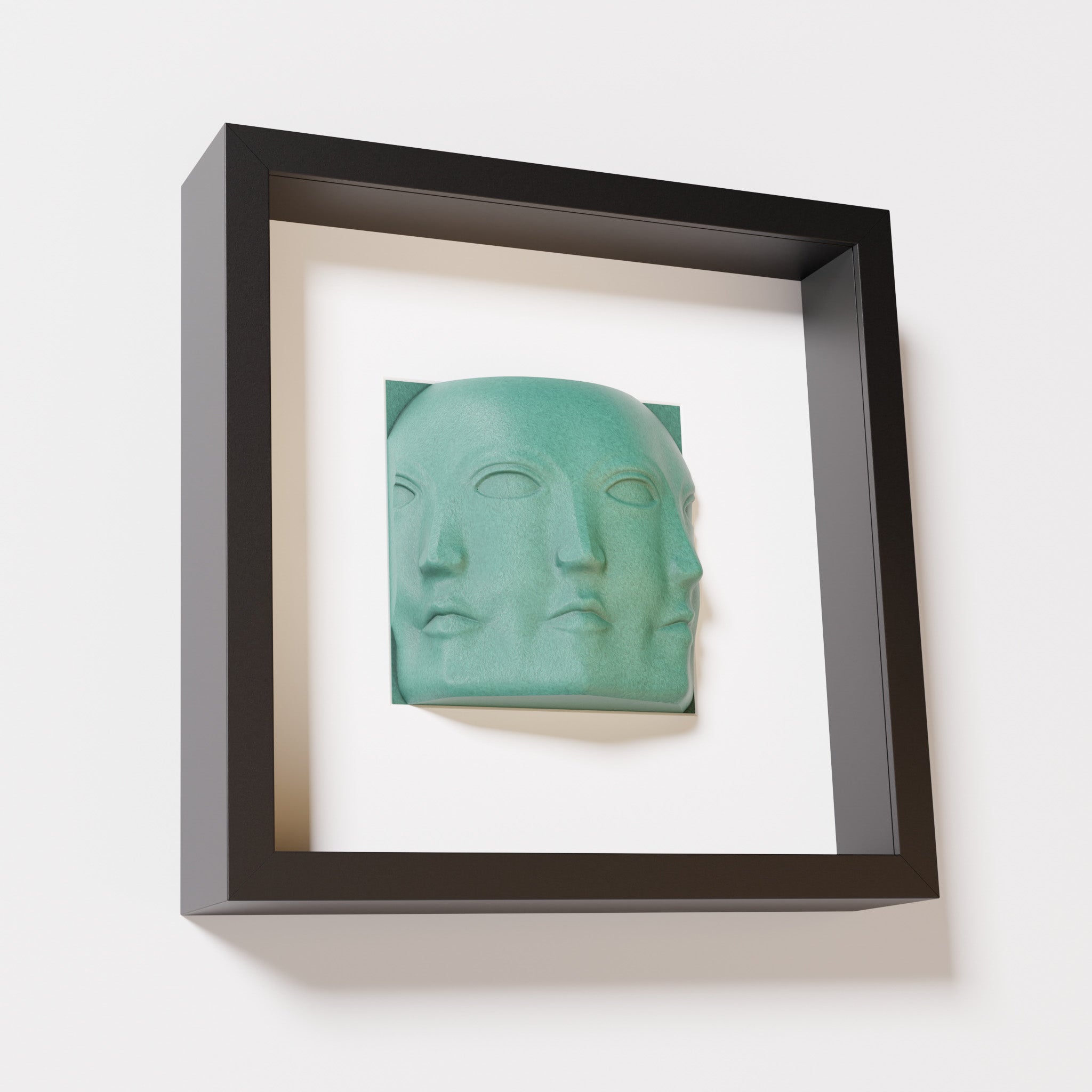 A close-up of a black shadowbox frame containing an old patina sculpture of 'Dora,' featuring three interconnected faces merging at the edges, creating a surreal and multi-dimensional effect.