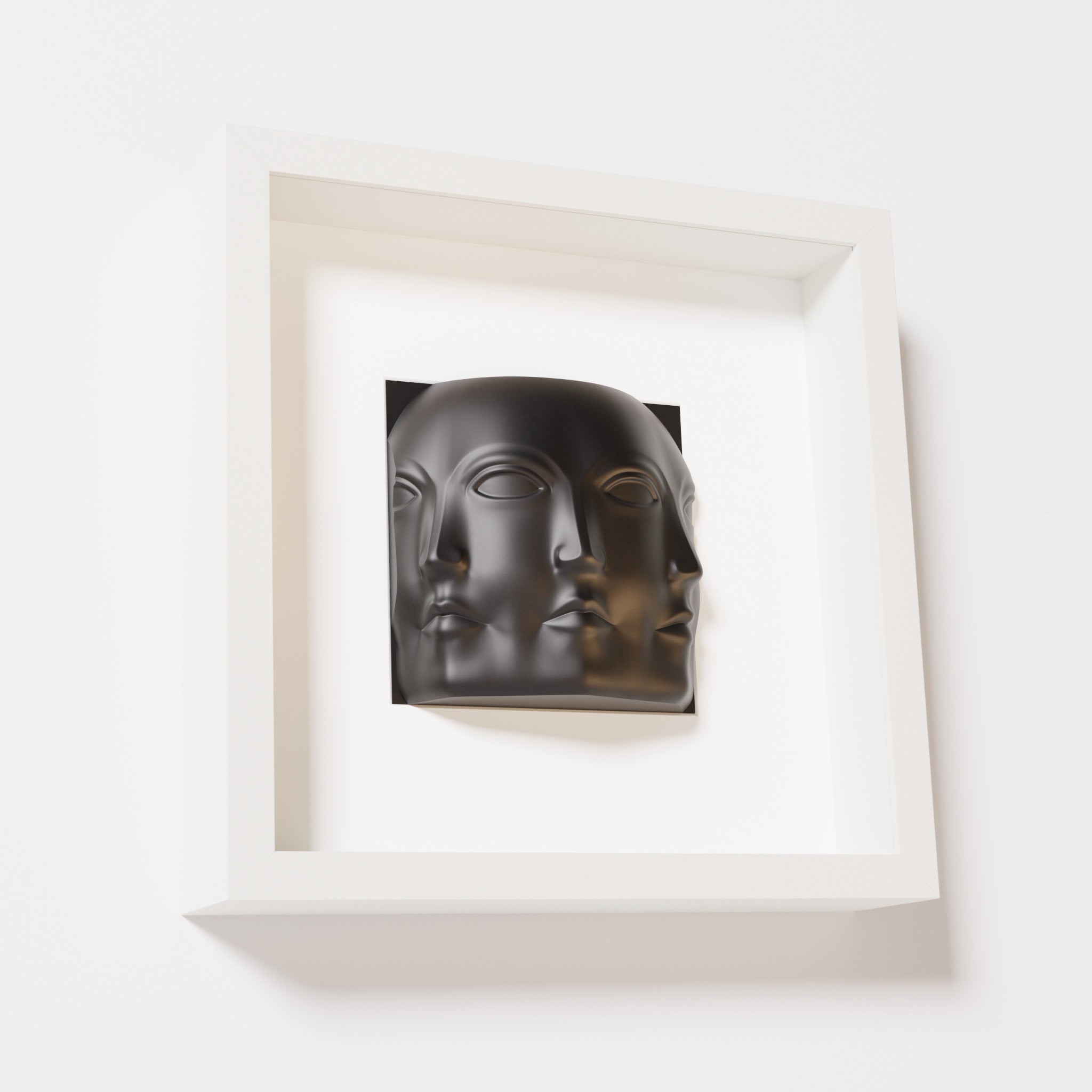 A close-up of a white shadowbox frame containing a matte black sculpture of 'Dora,' featuring three interconnected faces merging at the edges, creating a surreal and multi-dimensional effect.