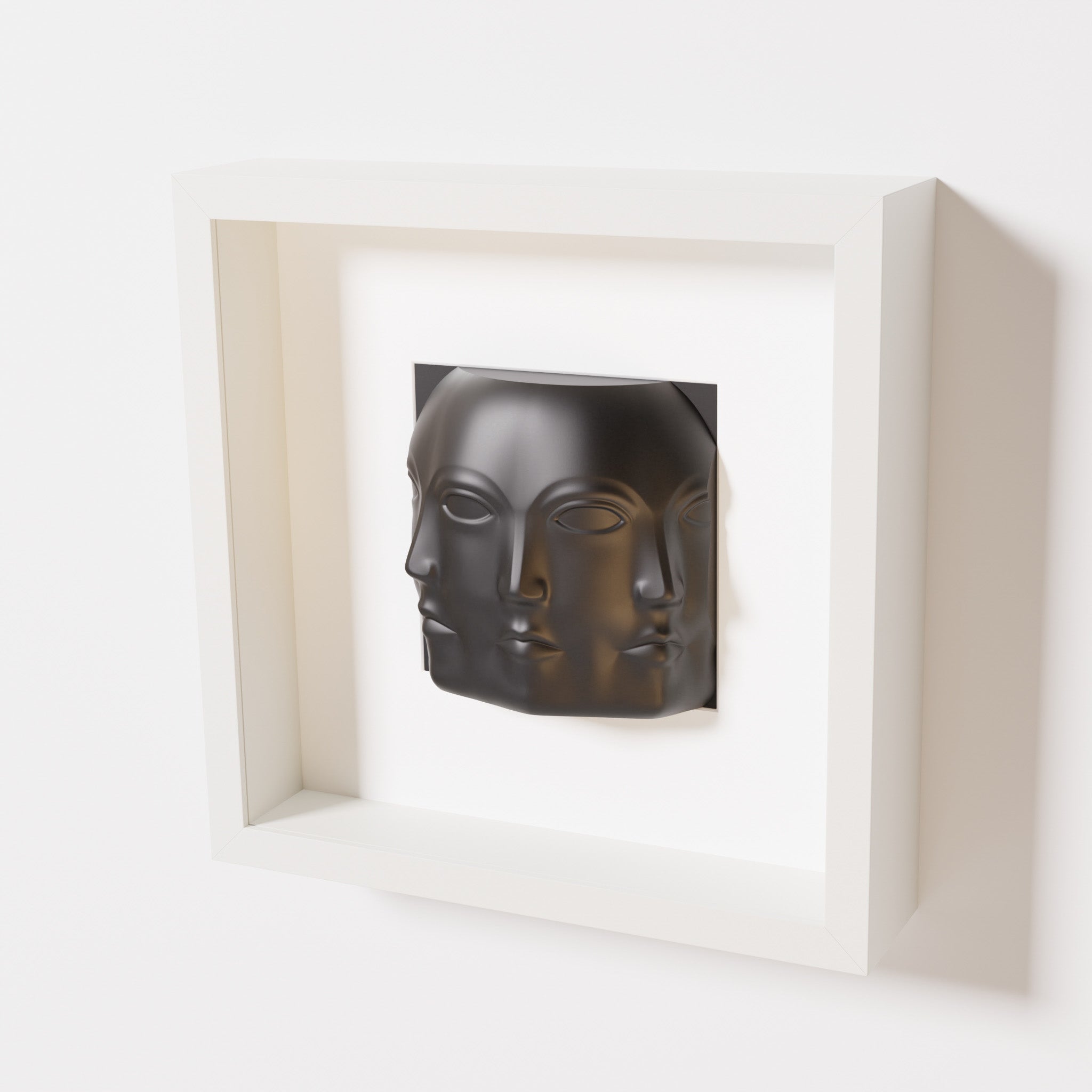 A close-up of a white shadowbox frame containing a matte black sculpture of 'Dora,' featuring three interconnected faces merging at the edges, creating a surreal and multi-dimensional effect.