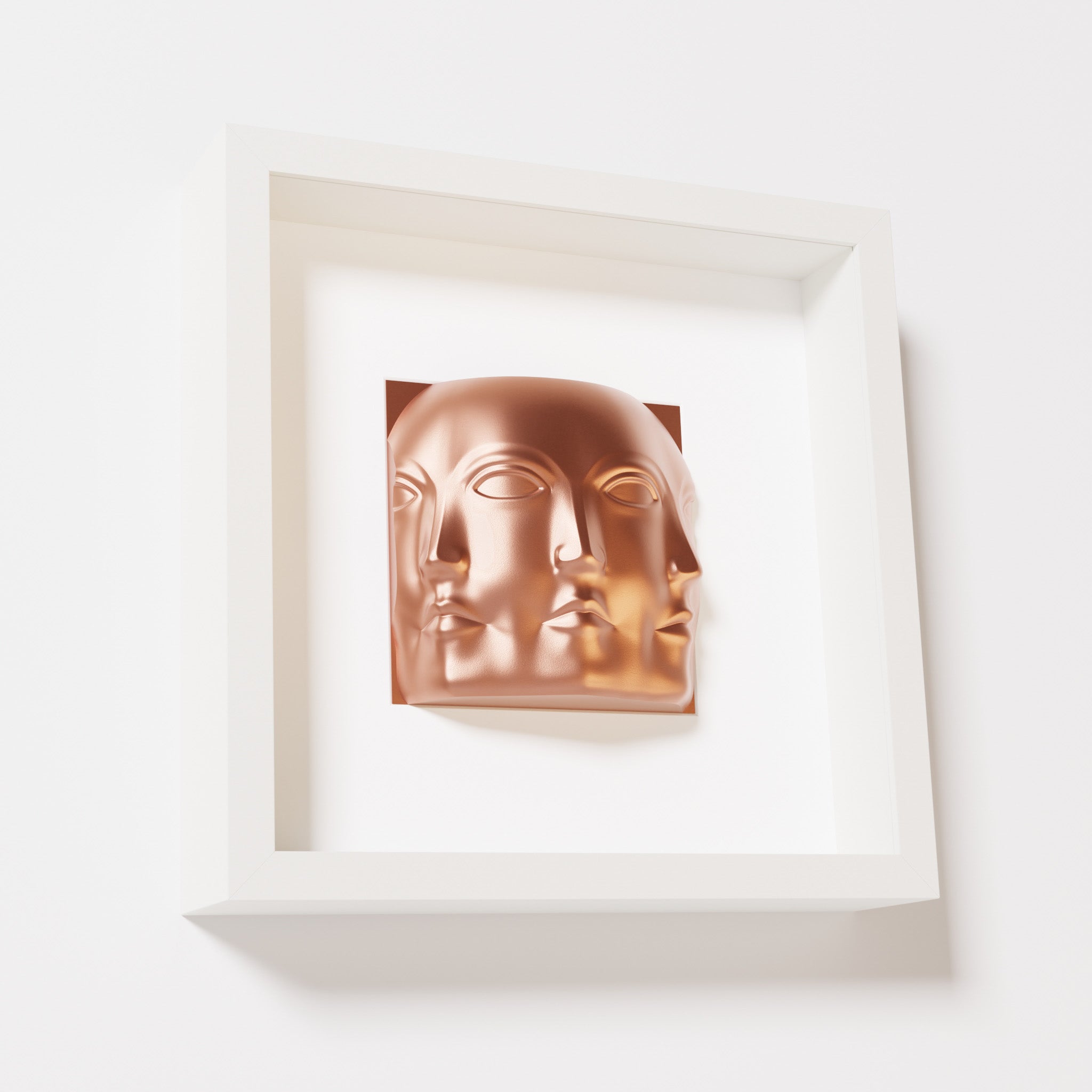 A close-up of a white shadowbox frame containing a chrome copper sculpture of 'Dora,' featuring three interconnected faces merging at the edges, creating a surreal and multi-dimensional effect.