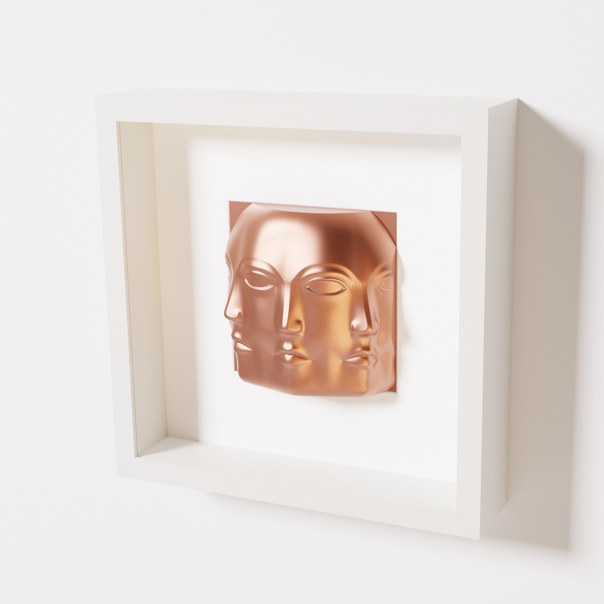 A close-up of a white shadowbox frame containing a chrome copper sculpture of 'Dora,' featuring three interconnected faces merging at the edges, creating a surreal and multi-dimensional effect.