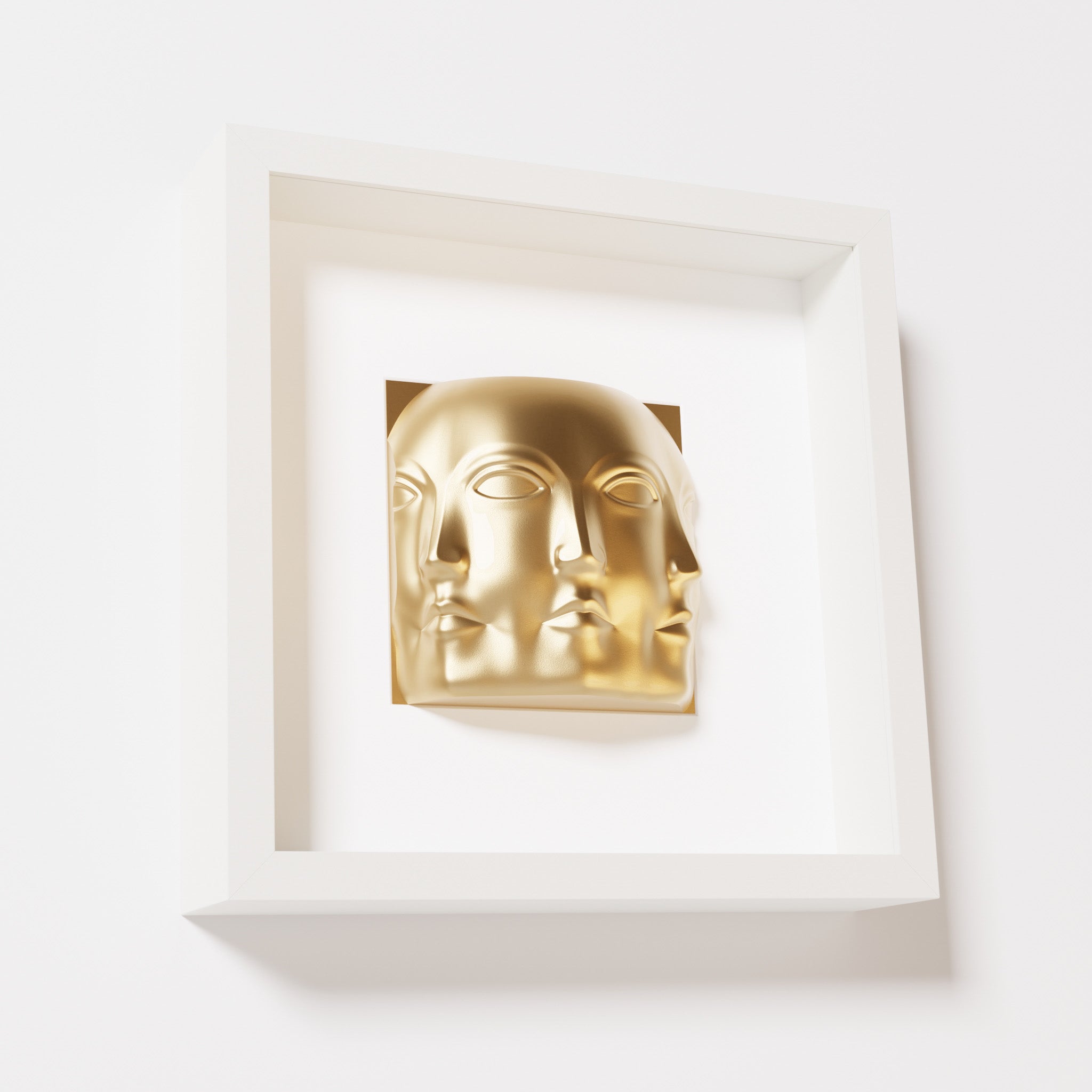 A close-up of a white shadowbox frame containing a chrome gold sculpture of 'Dora,' featuring three interconnected faces merging at the edges, creating a surreal and multi-dimensional effect.