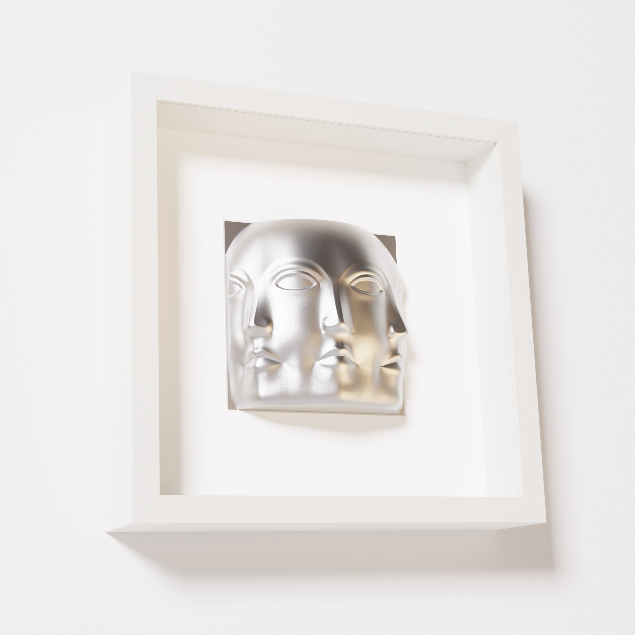 A close-up of a white shadowbox frame containing a chrome silver sculpture of 'Dora,' featuring three interconnected faces merging at the edges, creating a surreal and multi-dimensional effect.