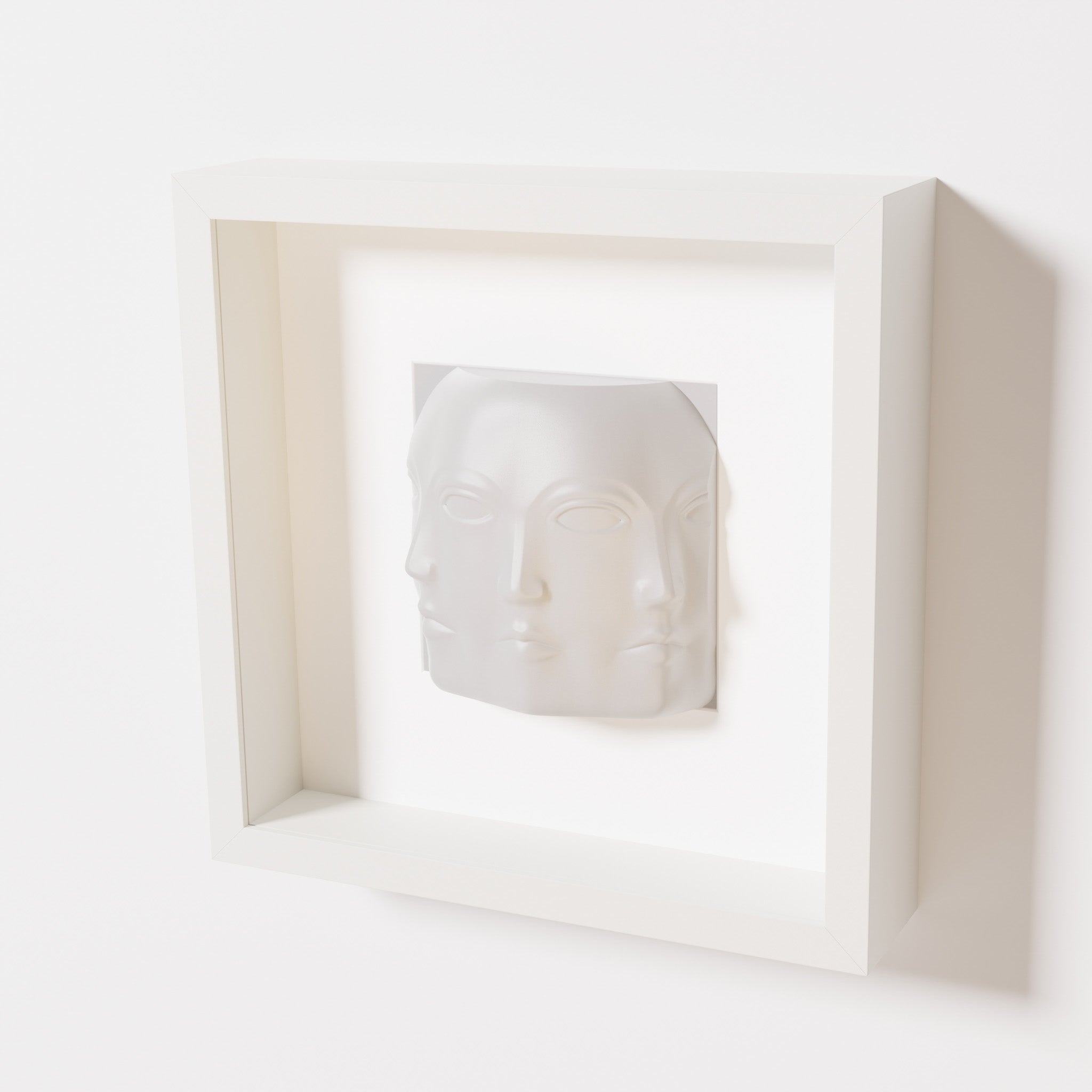 A close-up of a white shadowbox frame containing a marble white sculpture of 'Dora,' featuring three interconnected faces merging at the edges, creating a surreal and multi-dimensional effect.