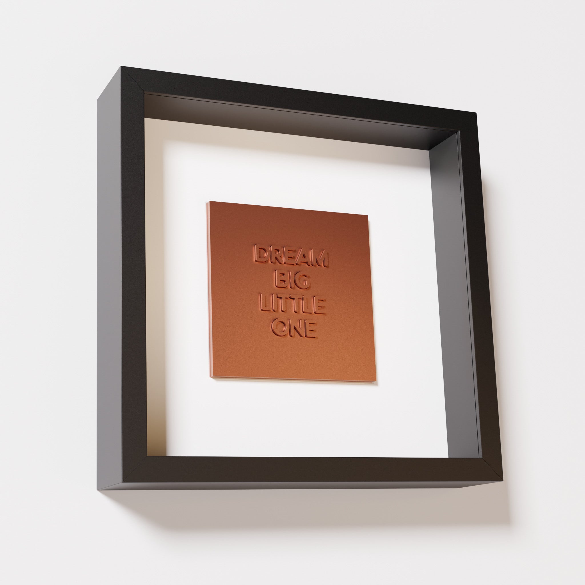 A close-up of a black shadowbox frame containing a chrome copper artwork with the phrase 'Dream big little one,' showcasing bold, raised lettering on a reflective copper surface.