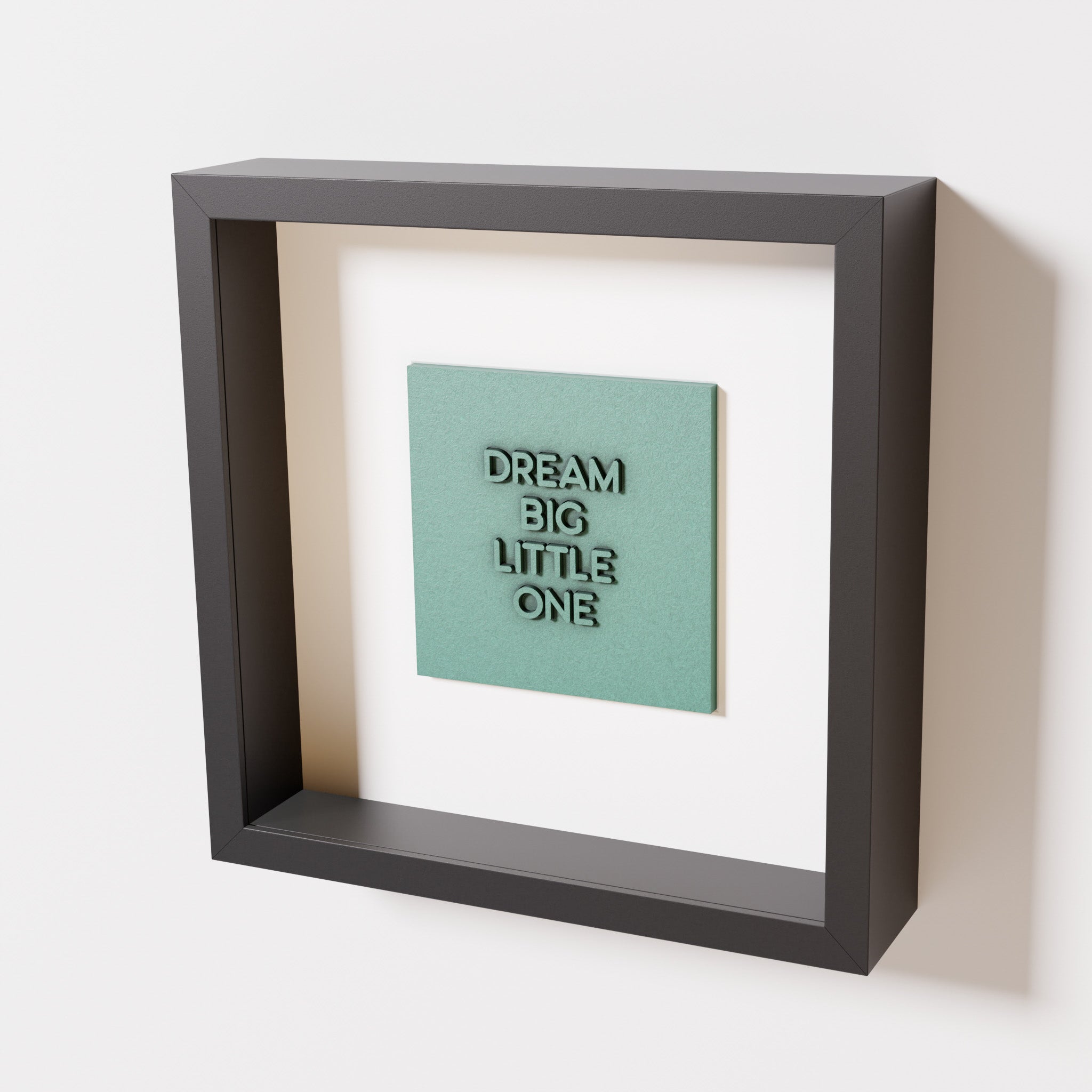 A close-up of a black shadowbox frame containing an old patina artwork with the phrase 'Dream big little one,' showcasing bold, raised lettering on a textured green surface.