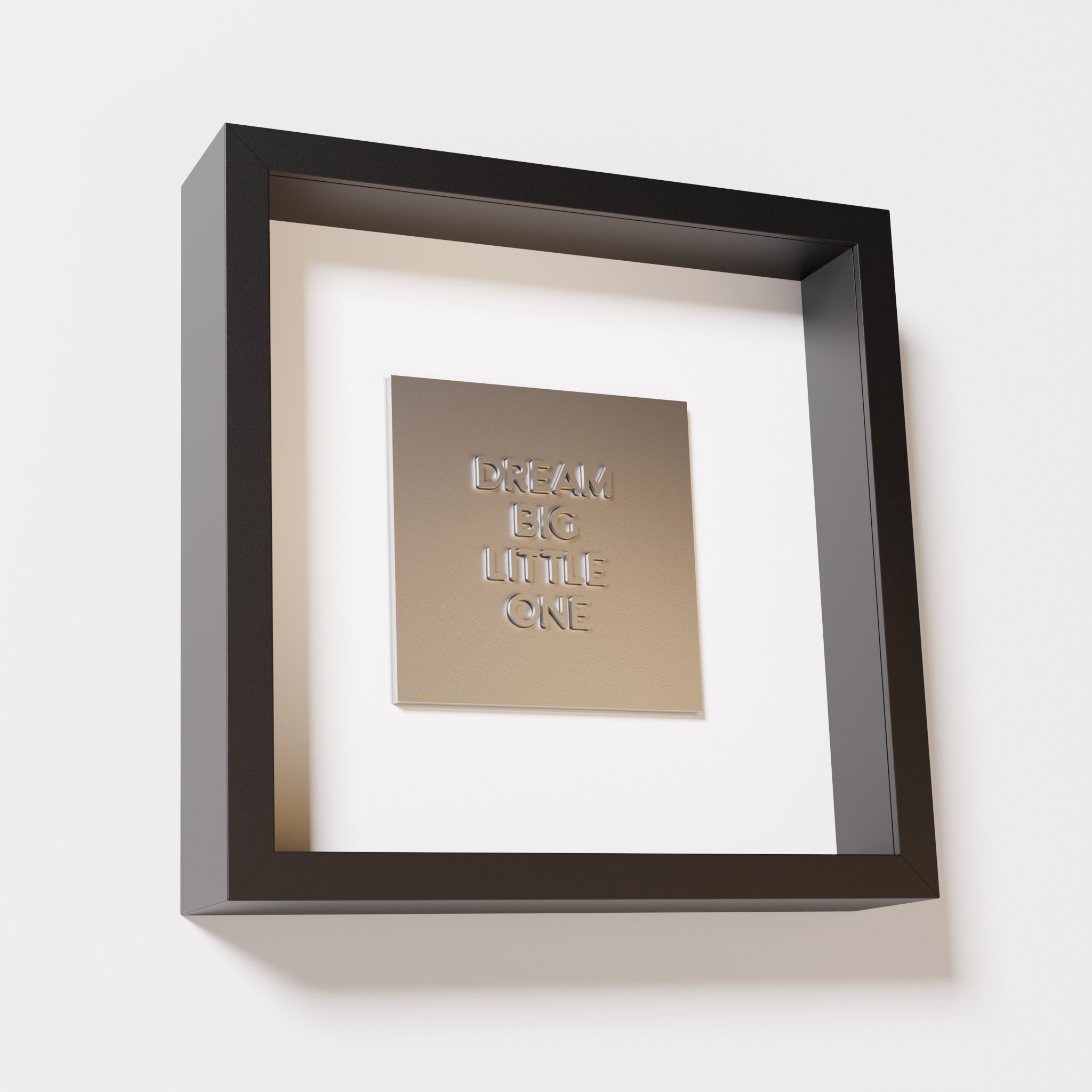 A close-up of a black shadowbox frame containing a chrome silver artwork with the phrase 'Dream big little one,' showcasing bold, raised lettering on a reflective silver surface.