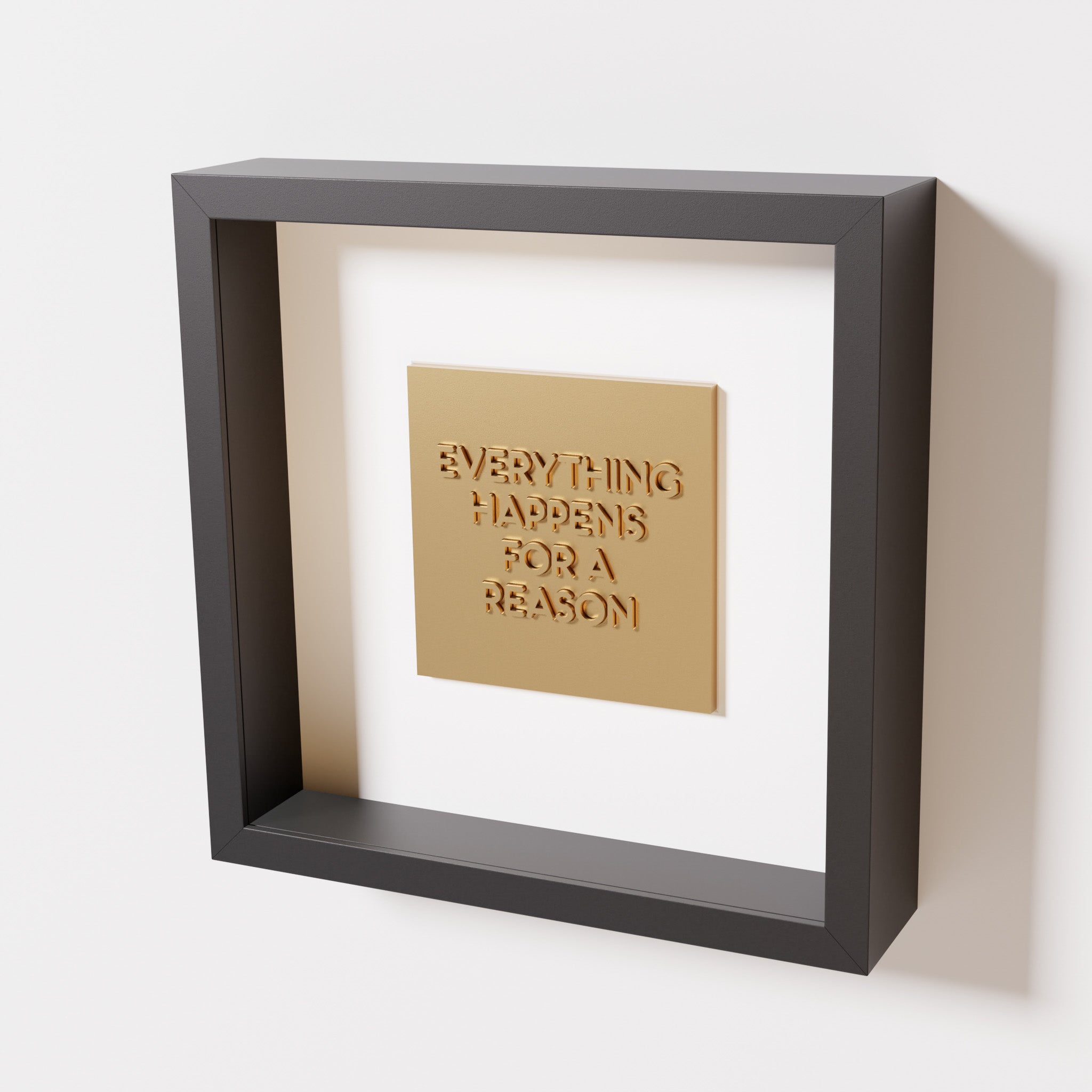 A close-up of a black shadowbox frame containing a chrome gold artwork featuring the thoughtful phrase 'Everything Happens for a Reason,' emphasizing its reflective golden highlights.