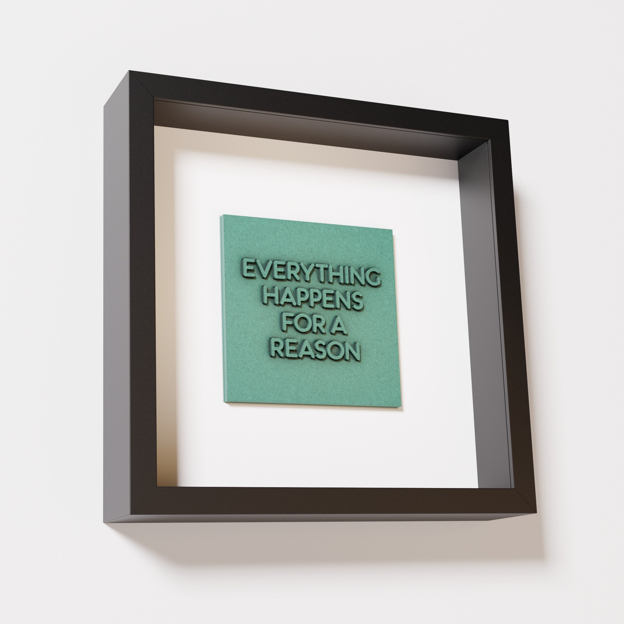 A close-up of a black shadowbox frame containing an old patina artwork featuring the thoughtful phrase 'Everything Happens for a Reason,' emphasizing its textured green finish and modern design.