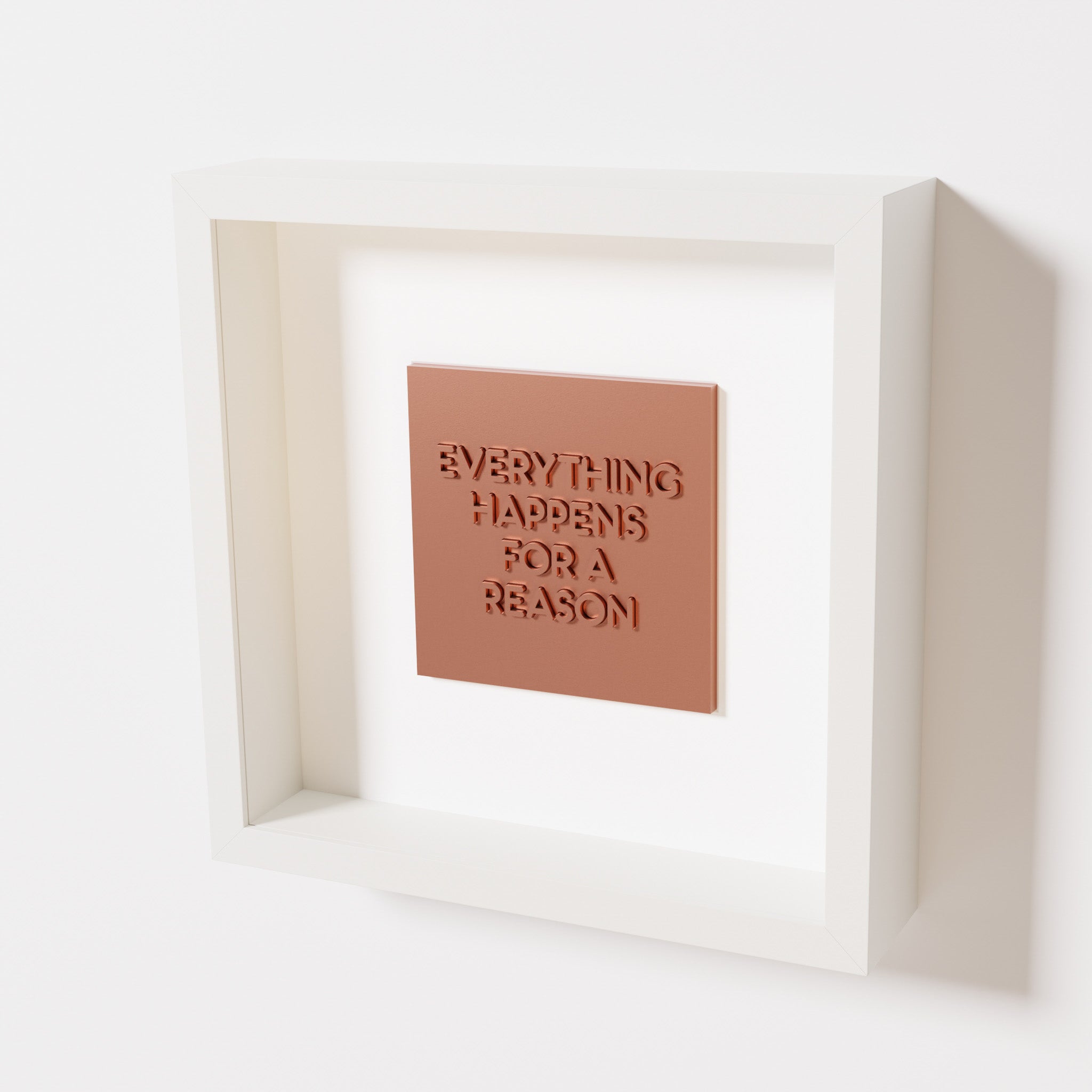 A close-up of a white shadowbox frame containing a chrome copper artwork featuring the thoughtful phrase 'Everything Happens for a Reason,' emphasizing its reflective copper highlights.