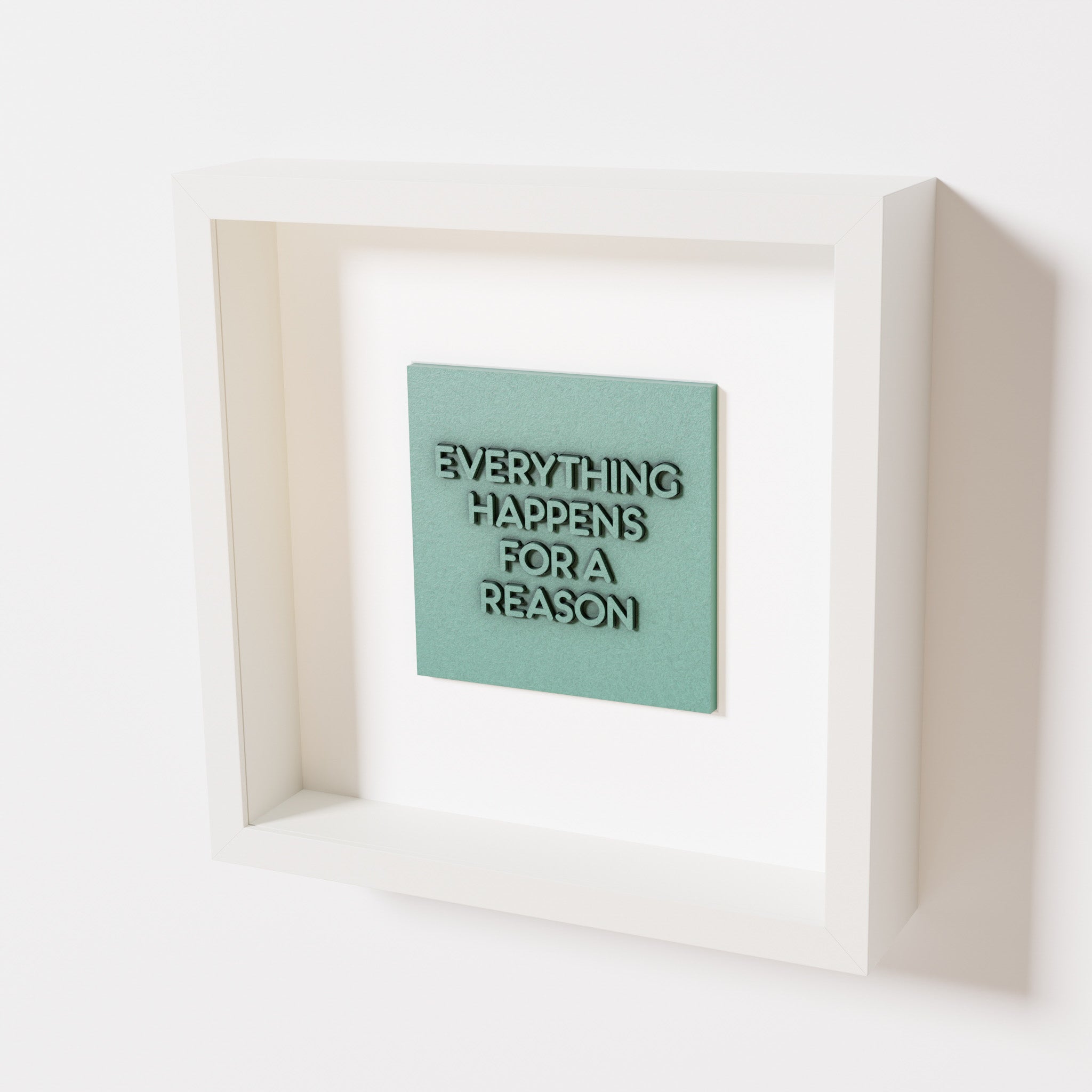 A close-up of a white shadowbox frame containing an old patina artwork featuring the thoughtful phrase 'Everything Happens for a Reason,' emphasizing its textured green finish and modern design.