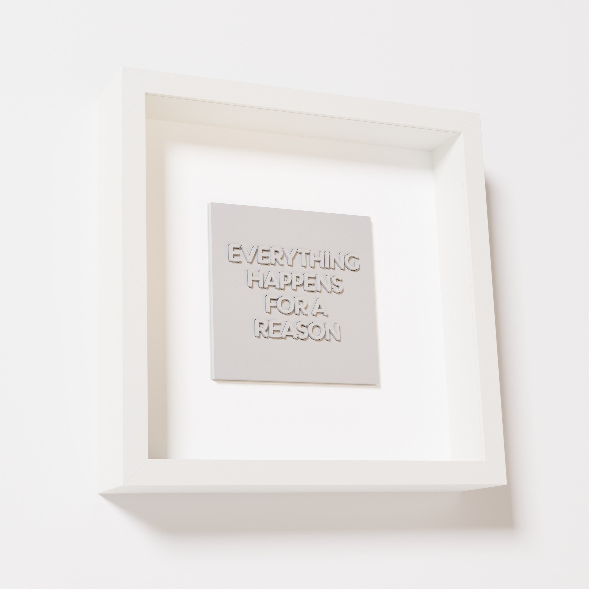 A close-up of a white shadowbox frame containing a marble white artwork featuring the thoughtful phrase 'Everything Happens for a Reason,' emphasizing its intricate text and modern design.