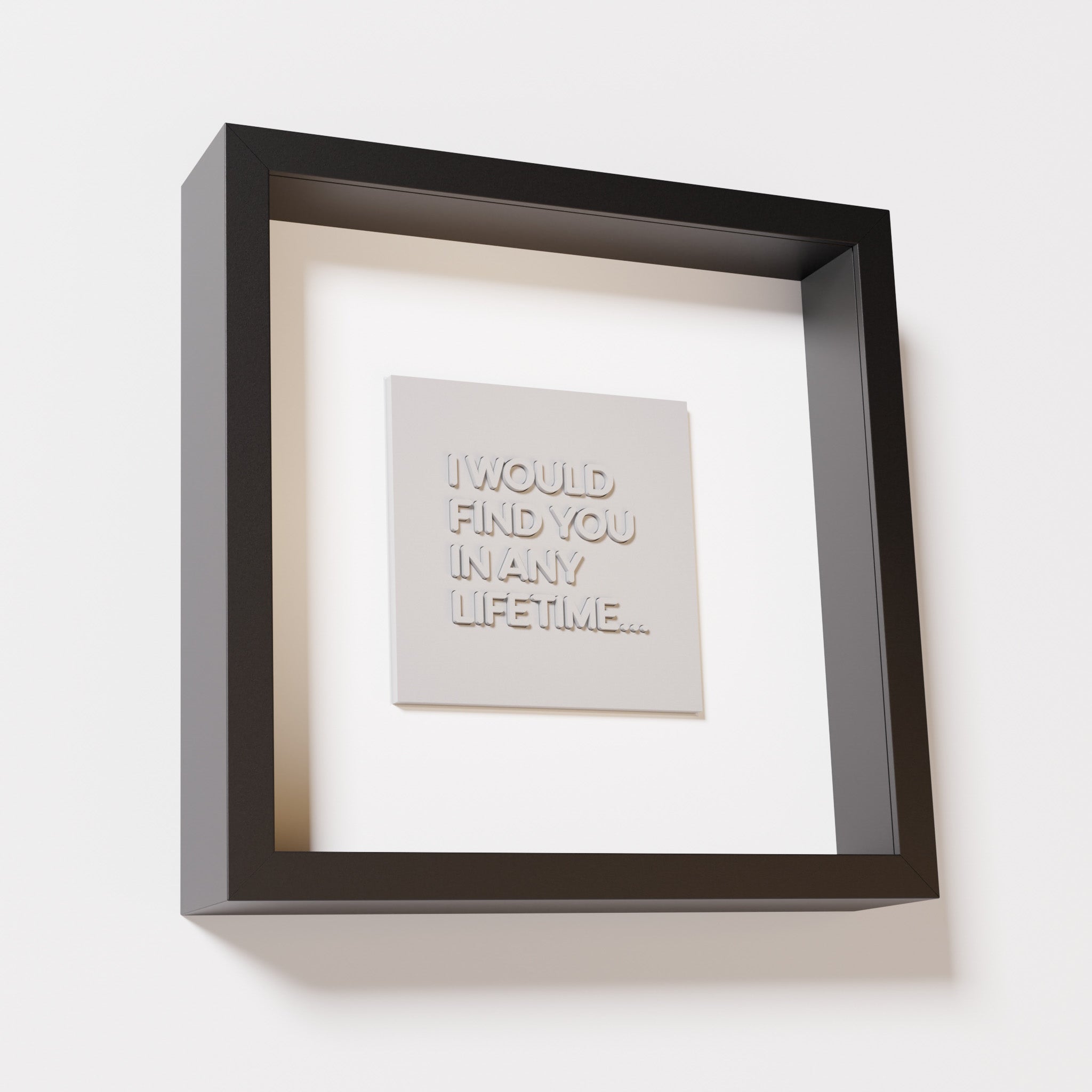 A close-up of a black shadowbox frame containing a marble white artwork with the phrase 'I would find you in any lifetime...,' featuring bold, raised lettering on a smooth background.