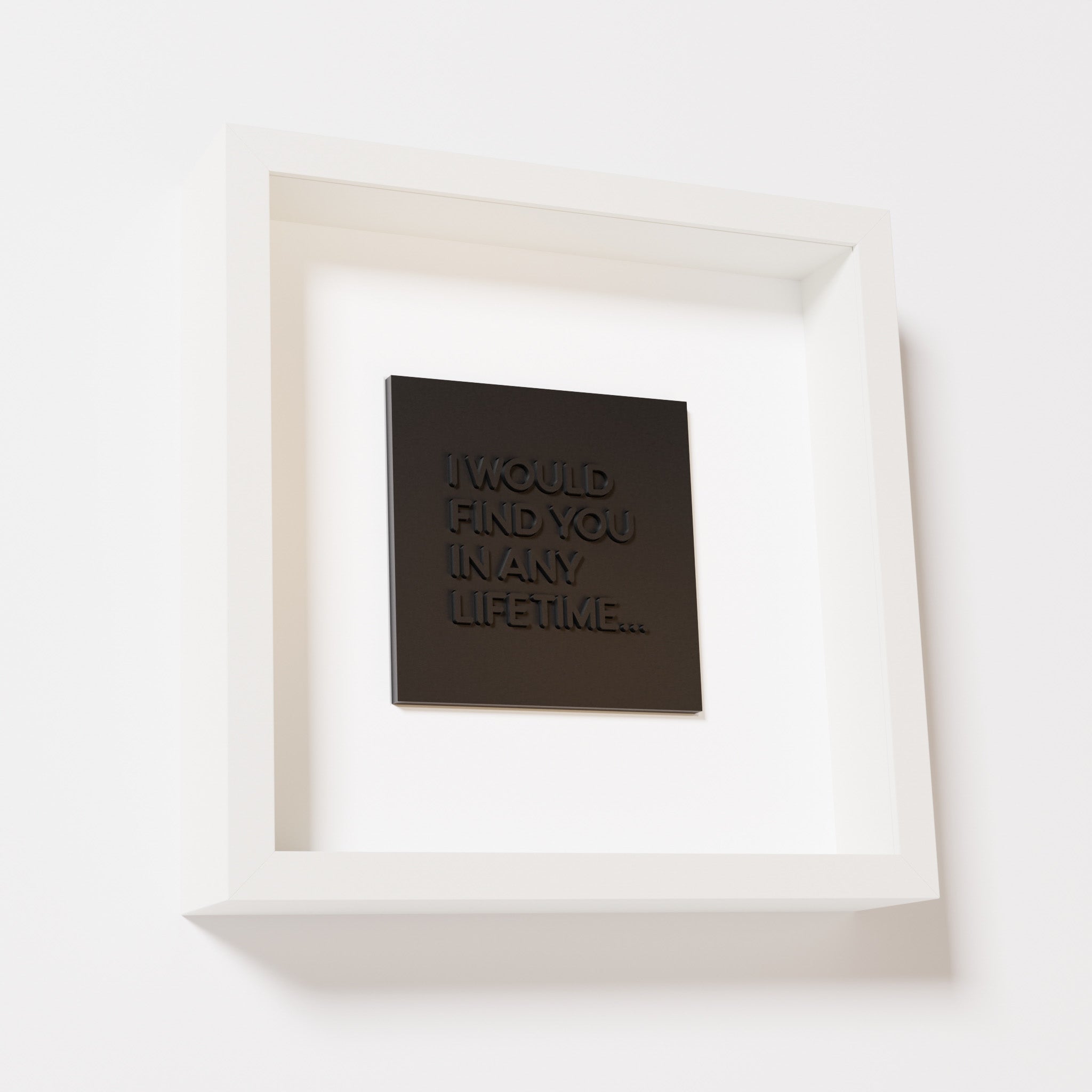 A close-up of a white shadowbox frame containing a matte black artwork with the phrase 'I would find you in any lifetime...,' featuring bold, raised lettering on a smooth background.