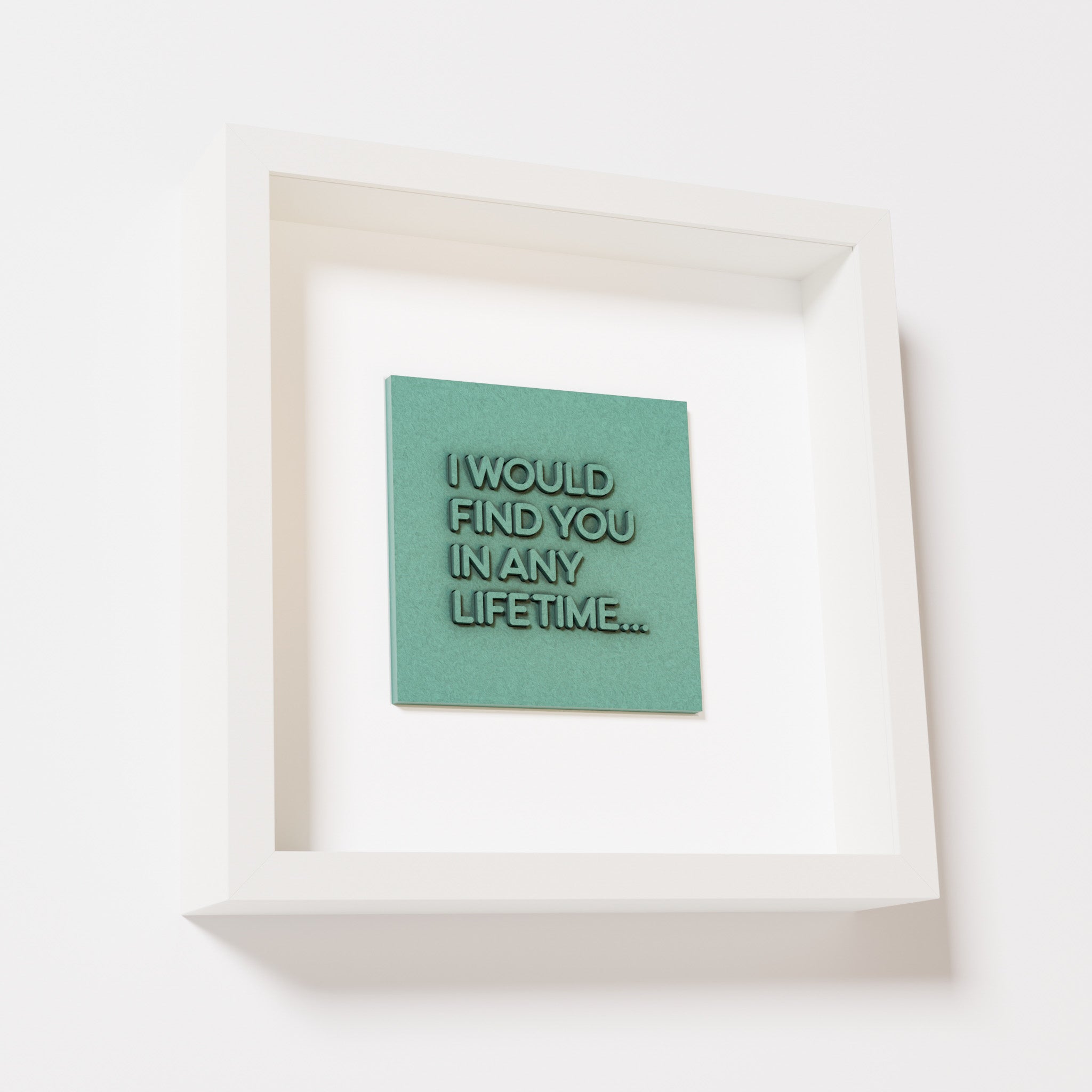 A close-up of a white shadowbox frame containing an old patina artwork with the phrase 'I would find you in any lifetime...,' featuring bold, raised lettering on a textured green surface.