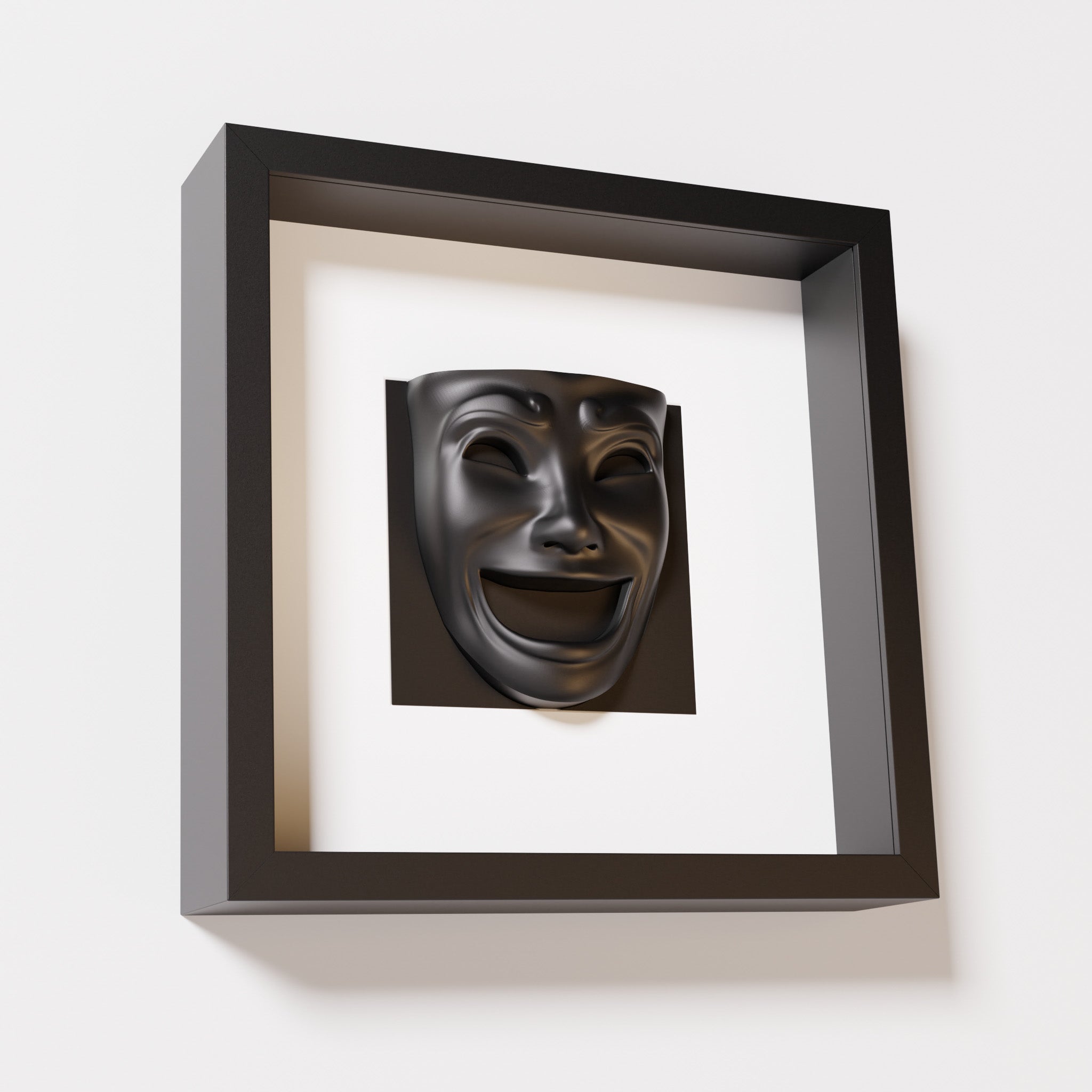 A close-up of a black shadowbox frame containing a matte black sculpture of 'Joy,' featuring a theatrical mask with a wide smile and expressive features, evoking happiness and positivity.