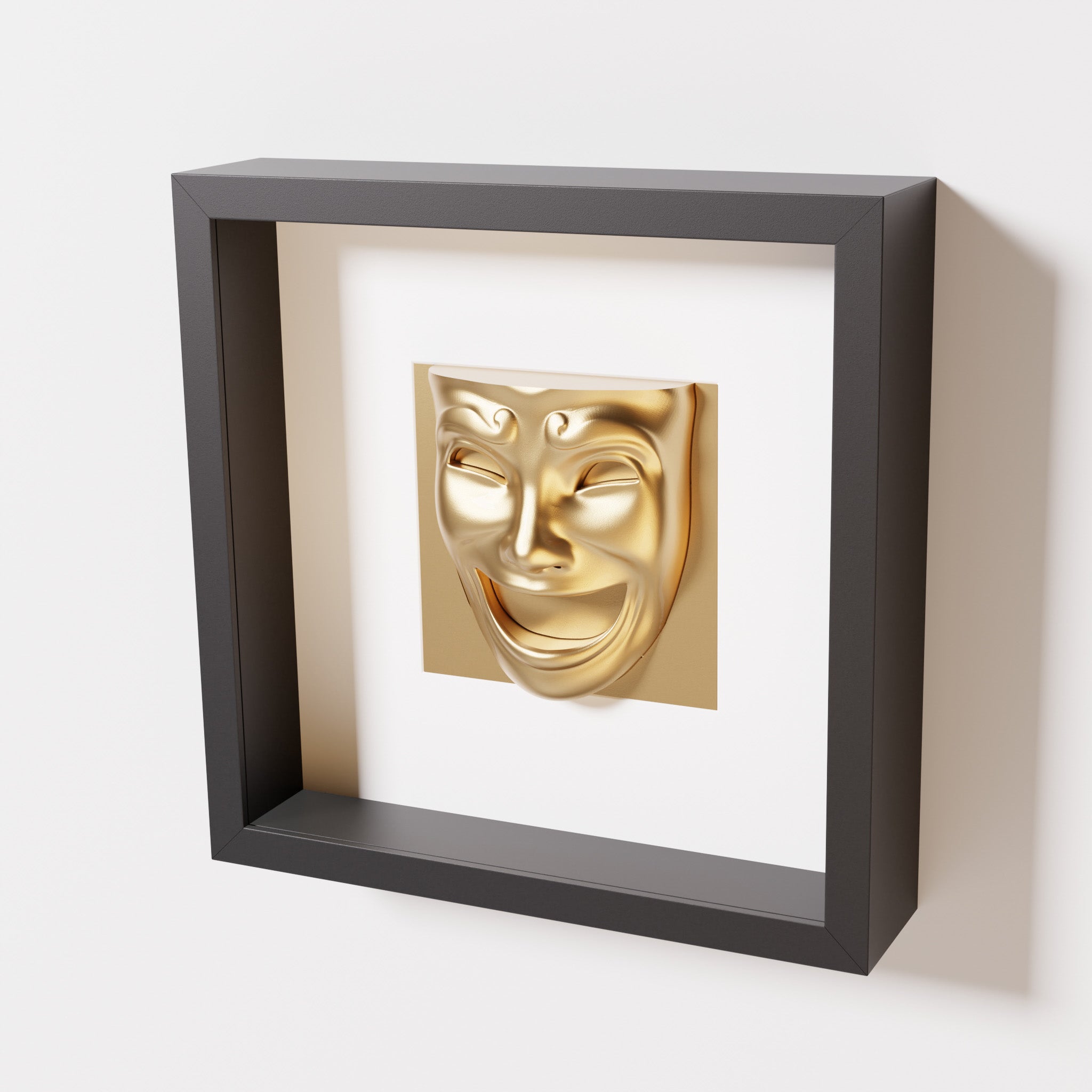 A close-up of a black shadowbox frame containing a chrome gold sculpture of 'Joy,' featuring a theatrical mask with a wide smile and expressive features, evoking happiness and positivity.