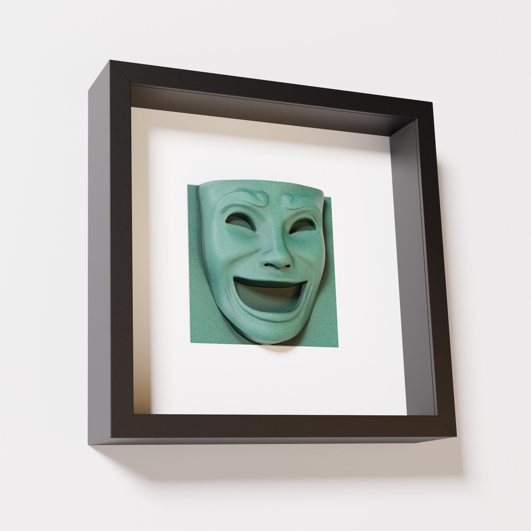 A close-up of a black shadowbox frame containing an old patina sculpture of 'Joy,' featuring a theatrical mask with a wide smile and expressive features, evoking happiness and positivity.