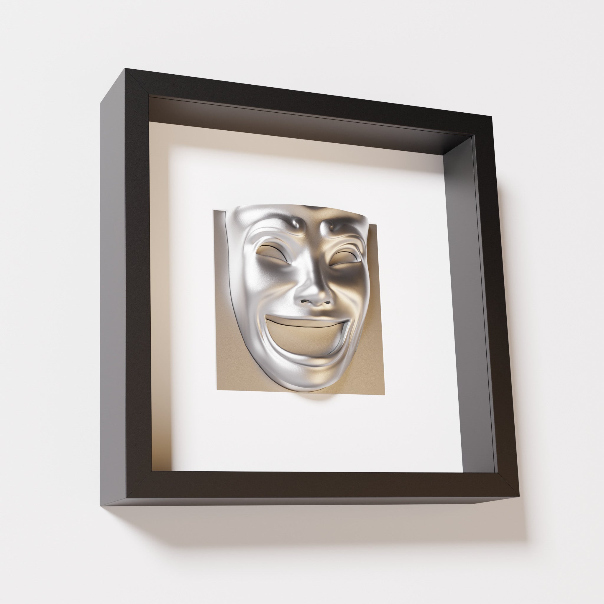 A close-up of a black shadowbox frame containing a chrome silver sculpture of 'Joy,' featuring a theatrical mask with a wide smile and expressive features, evoking happiness and positivity.