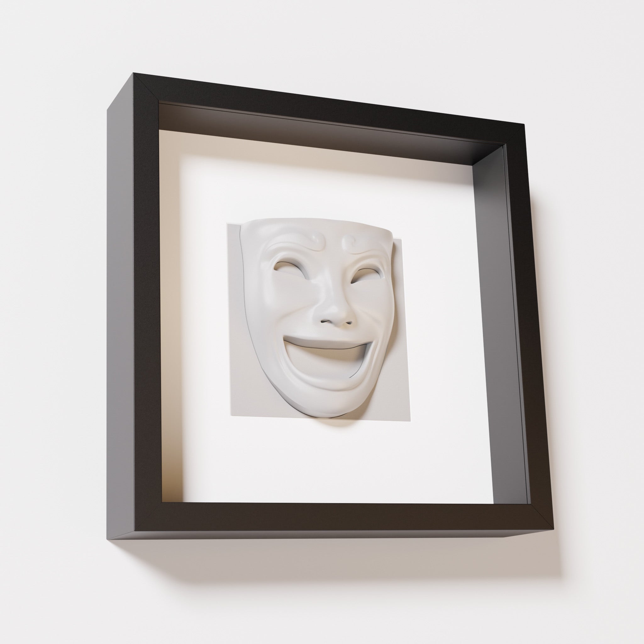 A close-up of a black shadowbox frame containing a marble white sculpture of 'Joy,' featuring a theatrical mask with a wide smile and expressive features, evoking happiness and positivity.