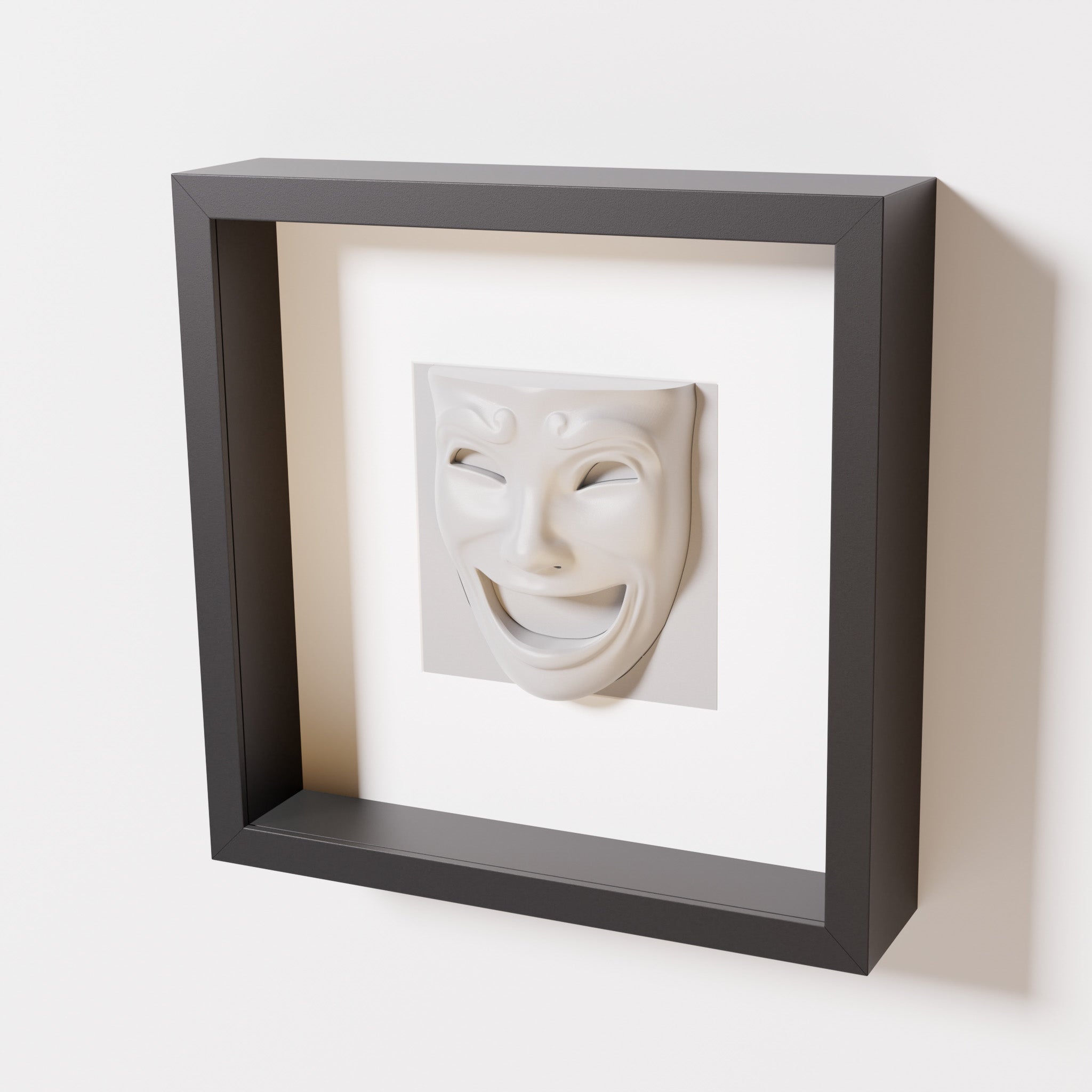 A close-up of a black shadowbox frame containing a marble white sculpture of 'Joy,' featuring a theatrical mask with a wide smile and expressive features, evoking happiness and positivity.