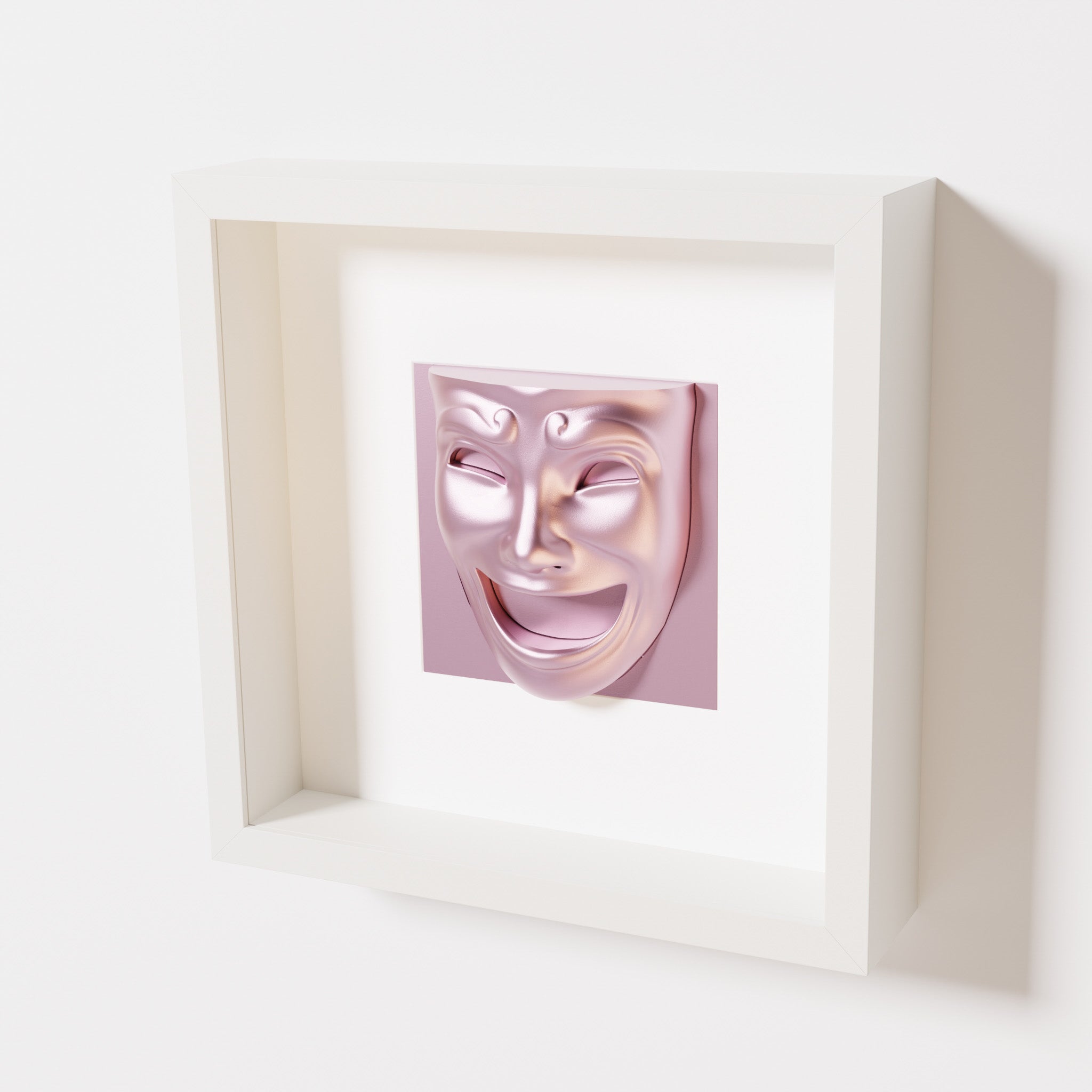 A close-up of a white shadowbox frame containing a metallic rose sculpture of 'Joy,' featuring a theatrical mask with a wide smile and expressive features, evoking happiness and positivity.