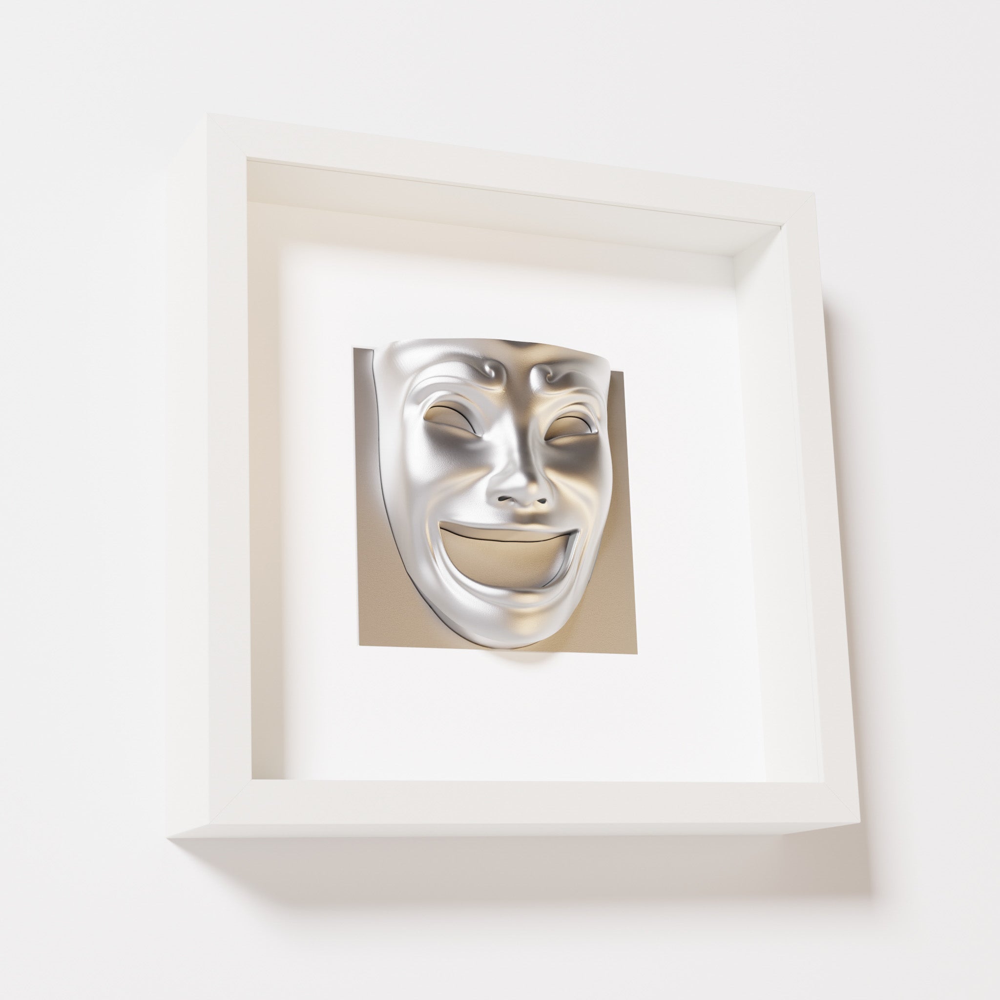 A close-up of a white shadowbox frame containing a chrome silver sculpture of 'Joy,' featuring a theatrical mask with a wide smile and expressive features, evoking happiness and positivity.