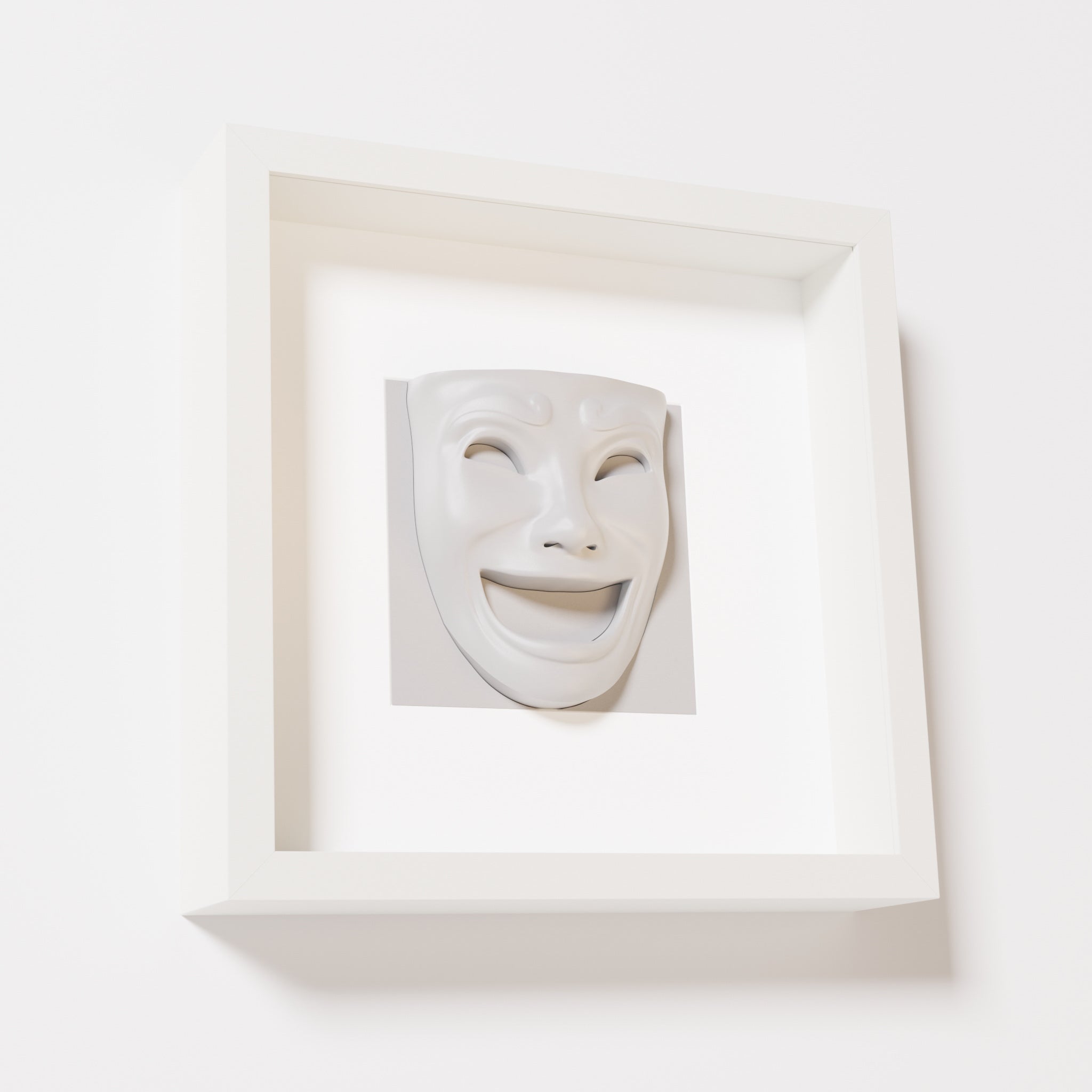 A close-up of a white shadowbox frame containing a marble white sculpture of 'Joy,' featuring a theatrical mask with a wide smile and expressive features, evoking happiness and positivity.