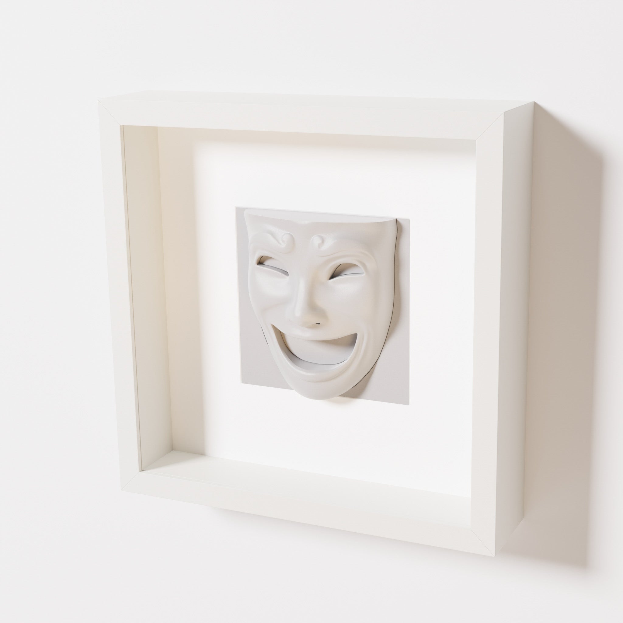 A close-up of a white shadowbox frame containing a marble white sculpture of 'Joy,' featuring a theatrical mask with a wide smile and expressive features, evoking happiness and positivity.