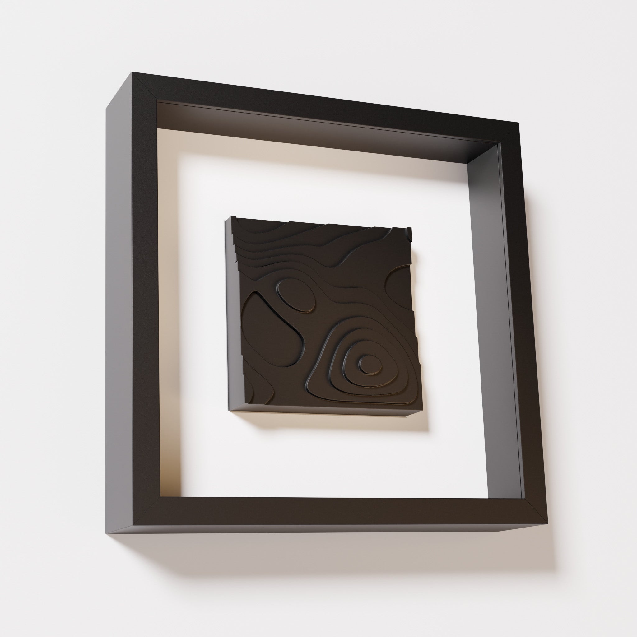 A close-up of a black shadowbox frame containing a matte black artwork depicting layered contour lines inspired by geographic elevation levels, showcasing intricate and geometric details.