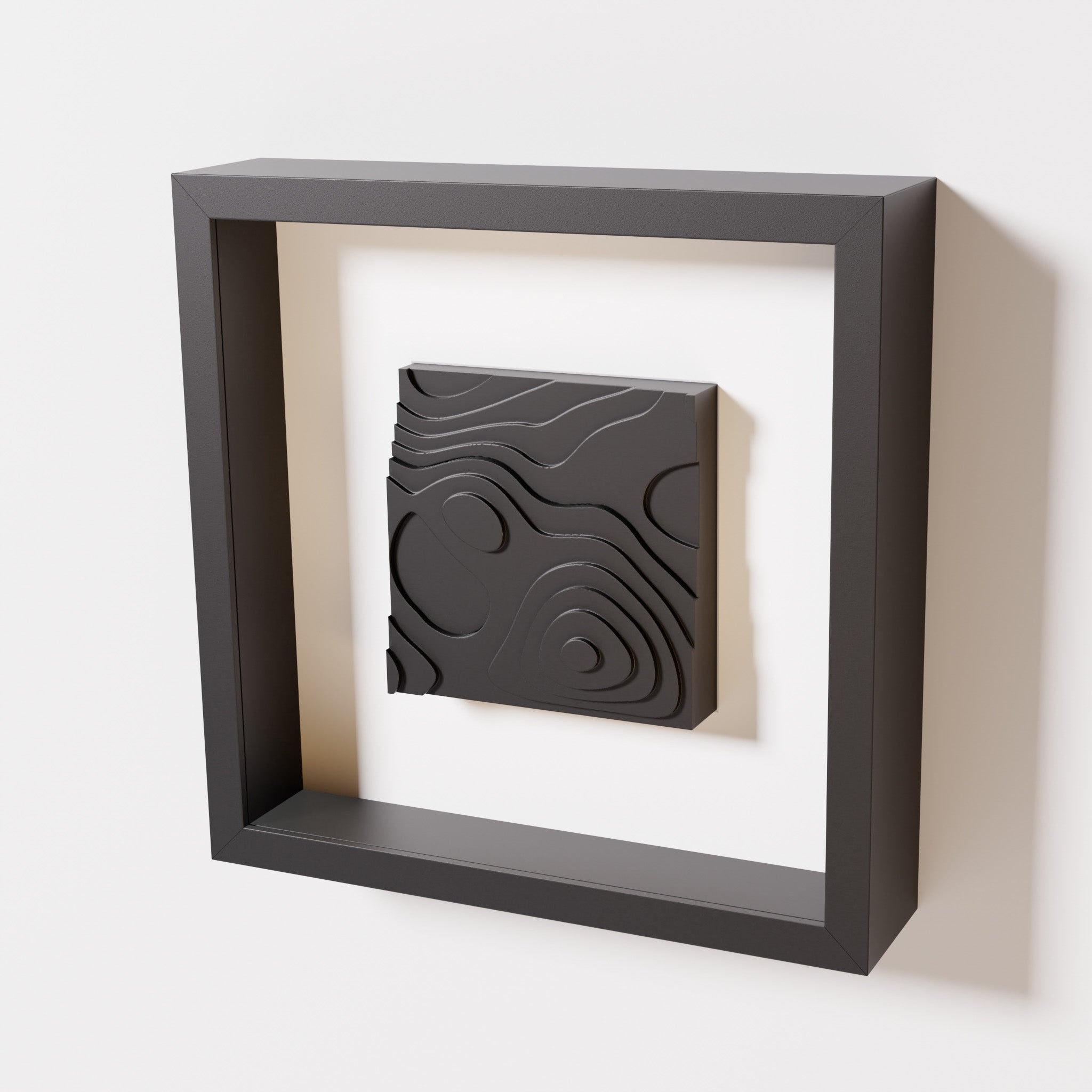 A close-up of a black shadowbox frame containing a matte black artwork depicting layered contour lines inspired by geographic elevation levels, showcasing intricate and geometric details.