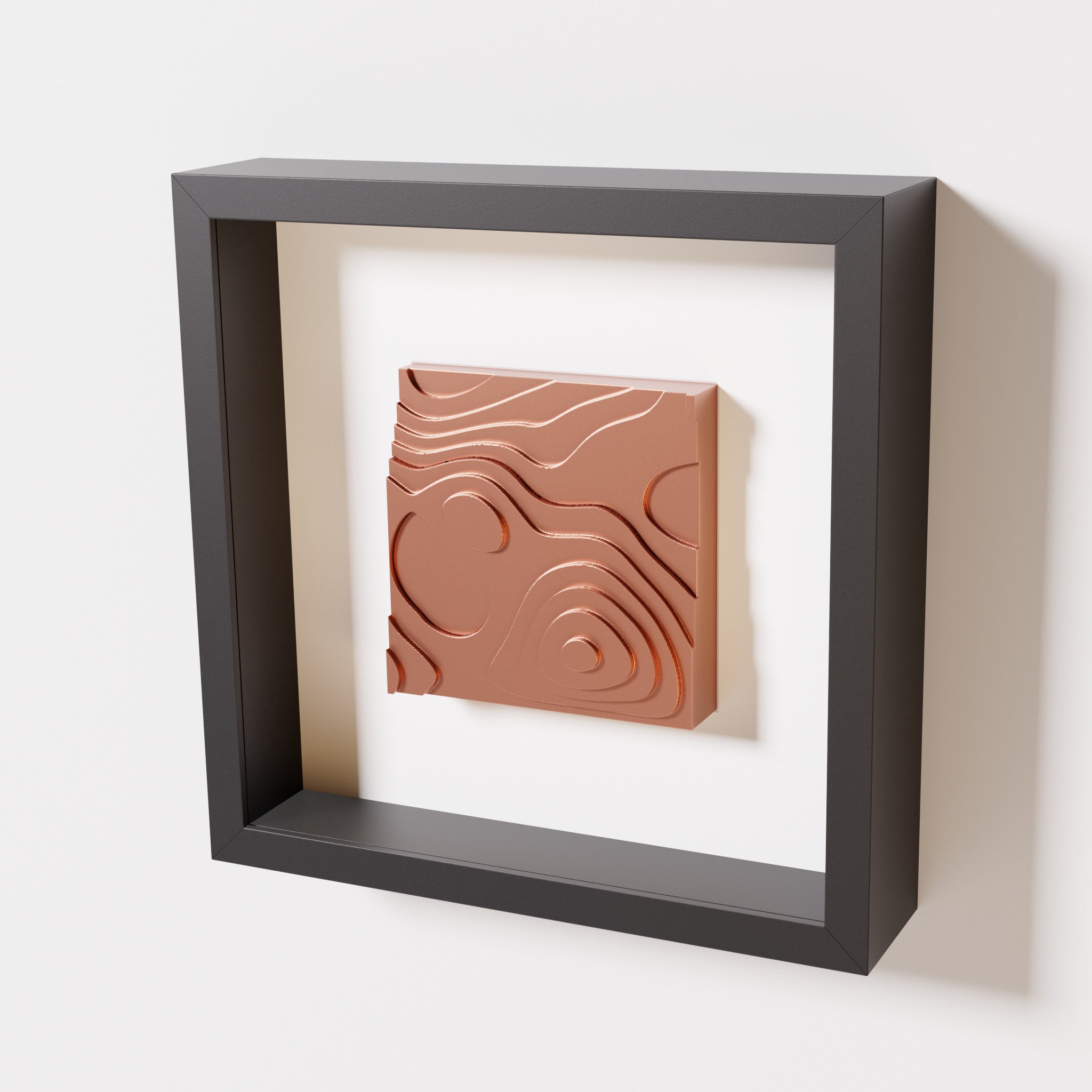 A close-up of a black shadowbox frame containing a chrome copper artwork depicting layered contour lines inspired by geographic elevation levels, showcasing reflective copper details.