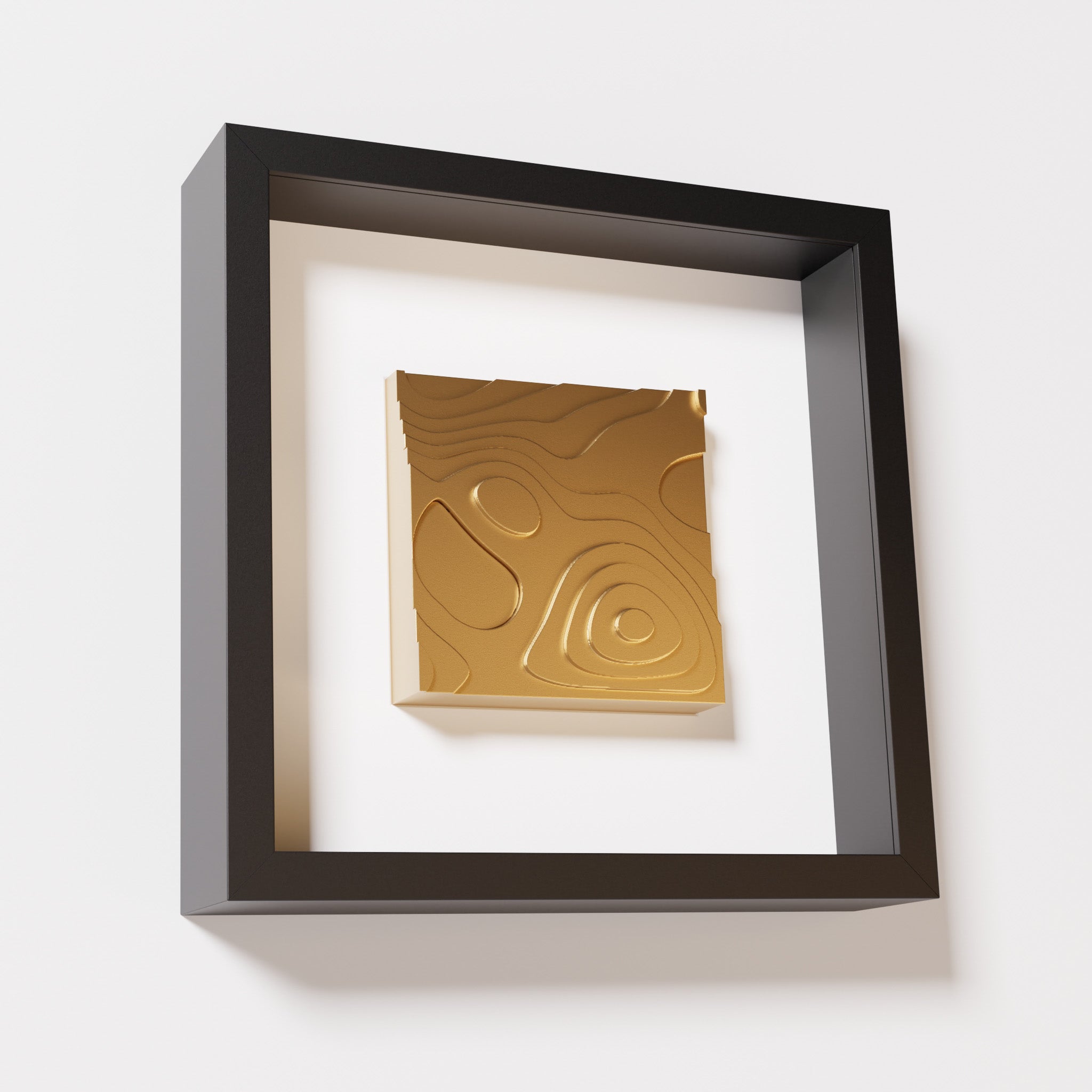 A close-up of a black shadowbox frame containing a chrome gold artwork depicting layered contour lines inspired by geographic elevation levels, showcasing reflective golden details.