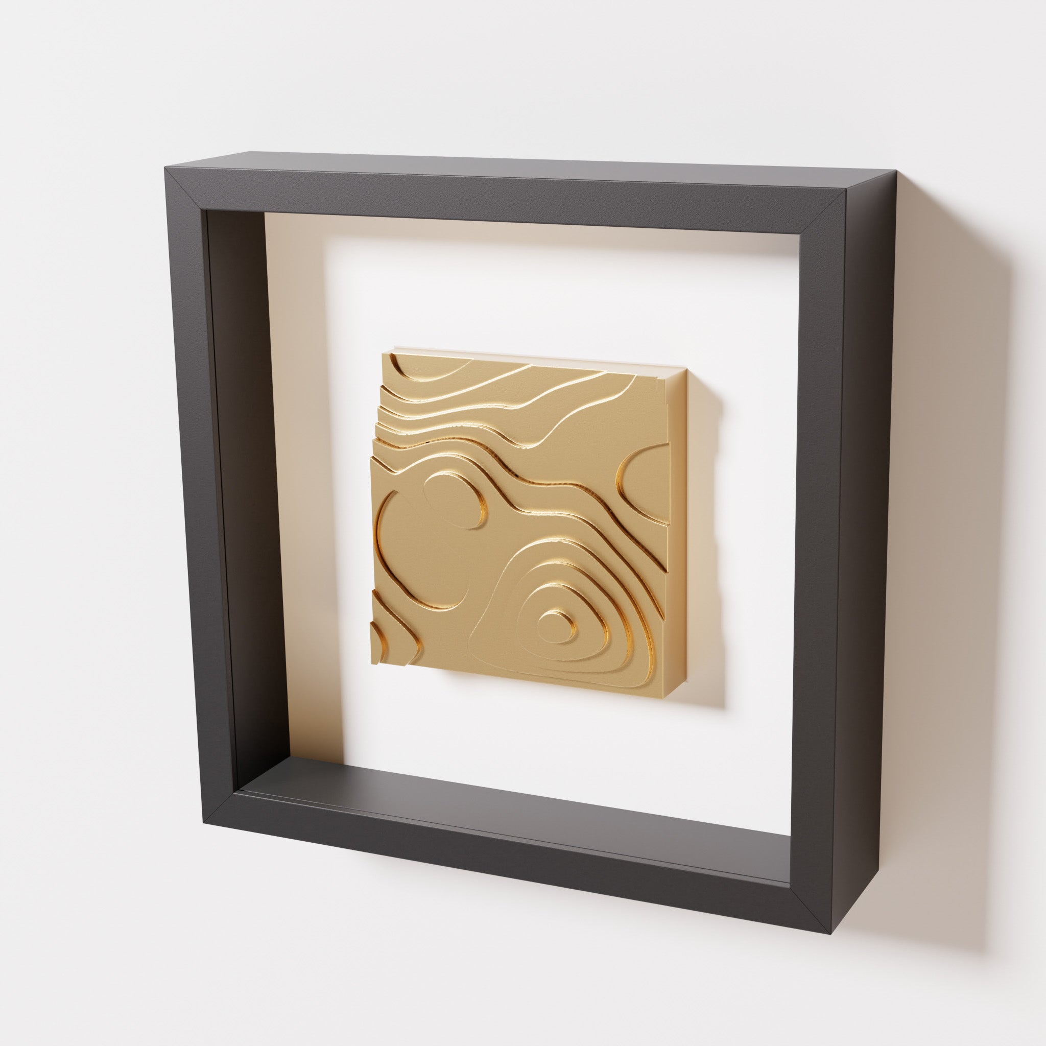 A close-up of a black shadowbox frame containing a chrome gold artwork depicting layered contour lines inspired by geographic elevation levels, showcasing reflective golden details.