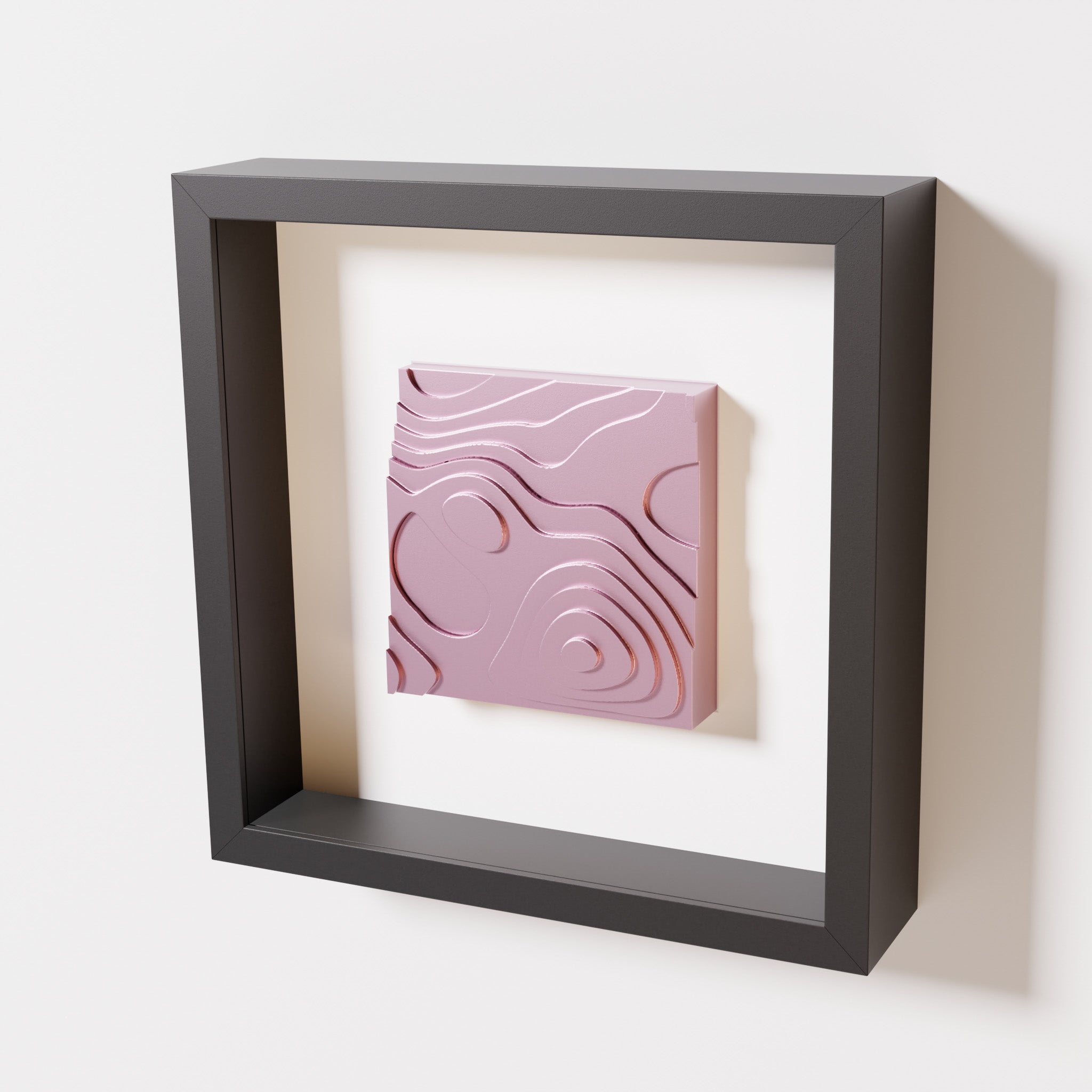 A close-up of a black shadowbox frame containing a metallic rose artwork depicting layered contour lines inspired by geographic elevation levels, showcasing reflective pink details.