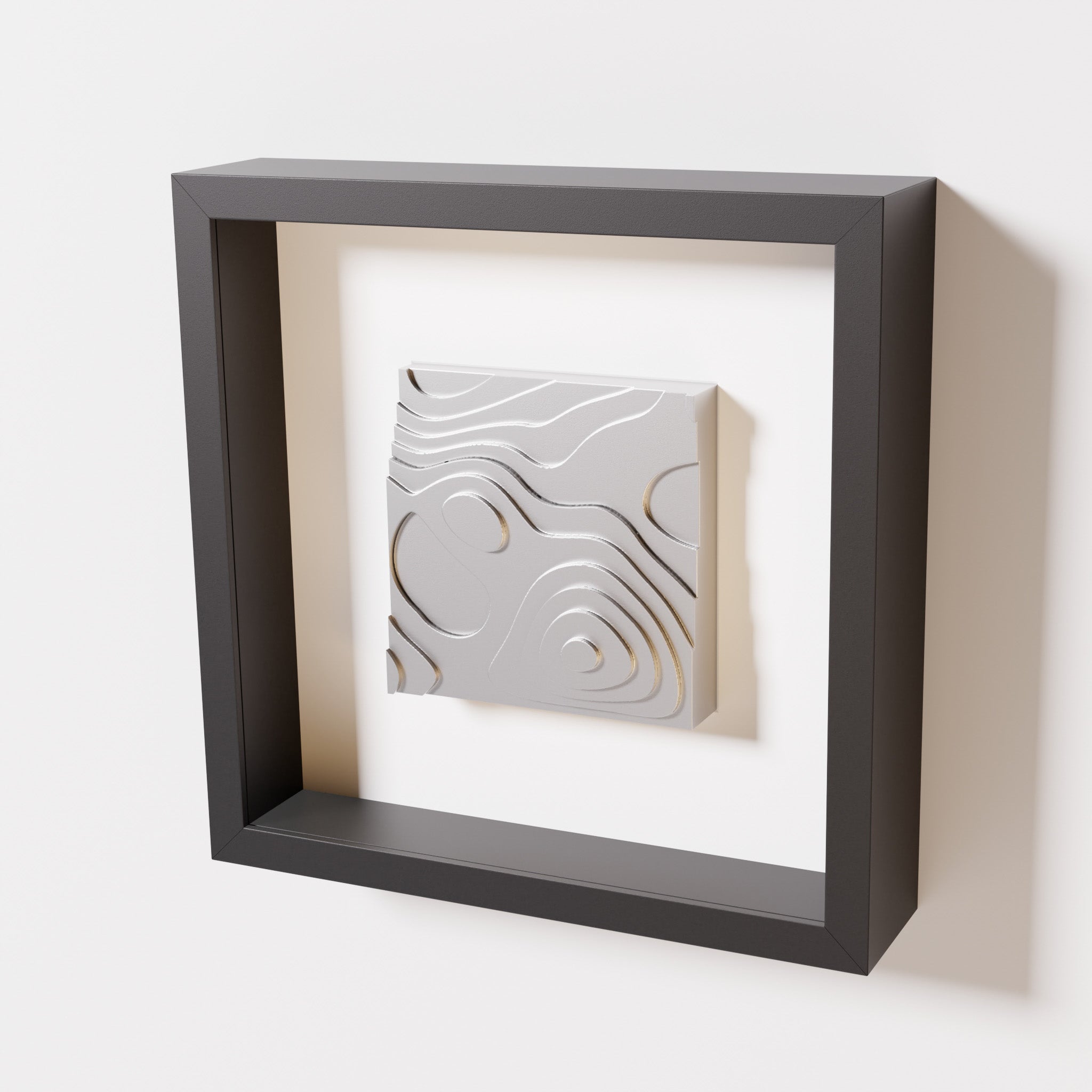 A close-up of a black shadowbox frame containing a chrome silver artwork depicting layered contour lines inspired by geographic elevation levels, showcasing reflective silver details.