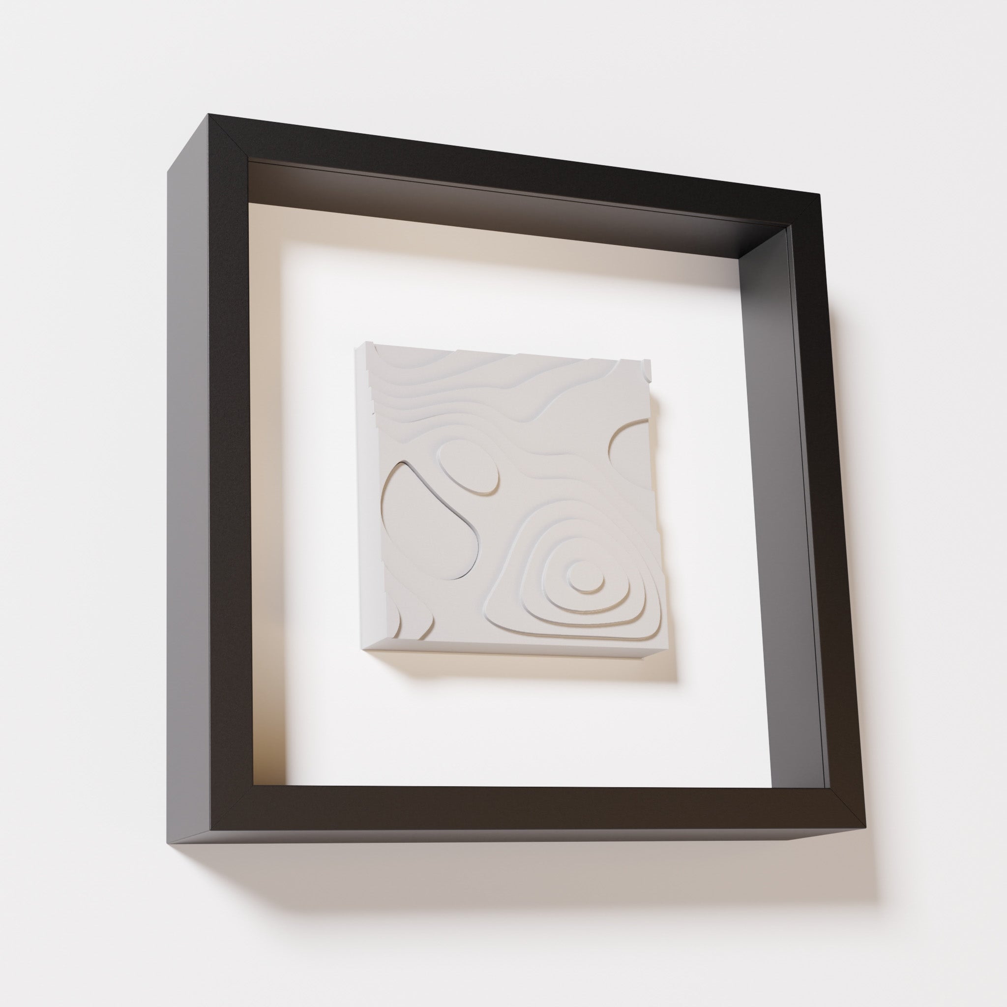 A close-up of a black shadowbox frame containing a marble white artwork depicting layered contour lines inspired by geographic elevation levels, showcasing intricate and geometric details.