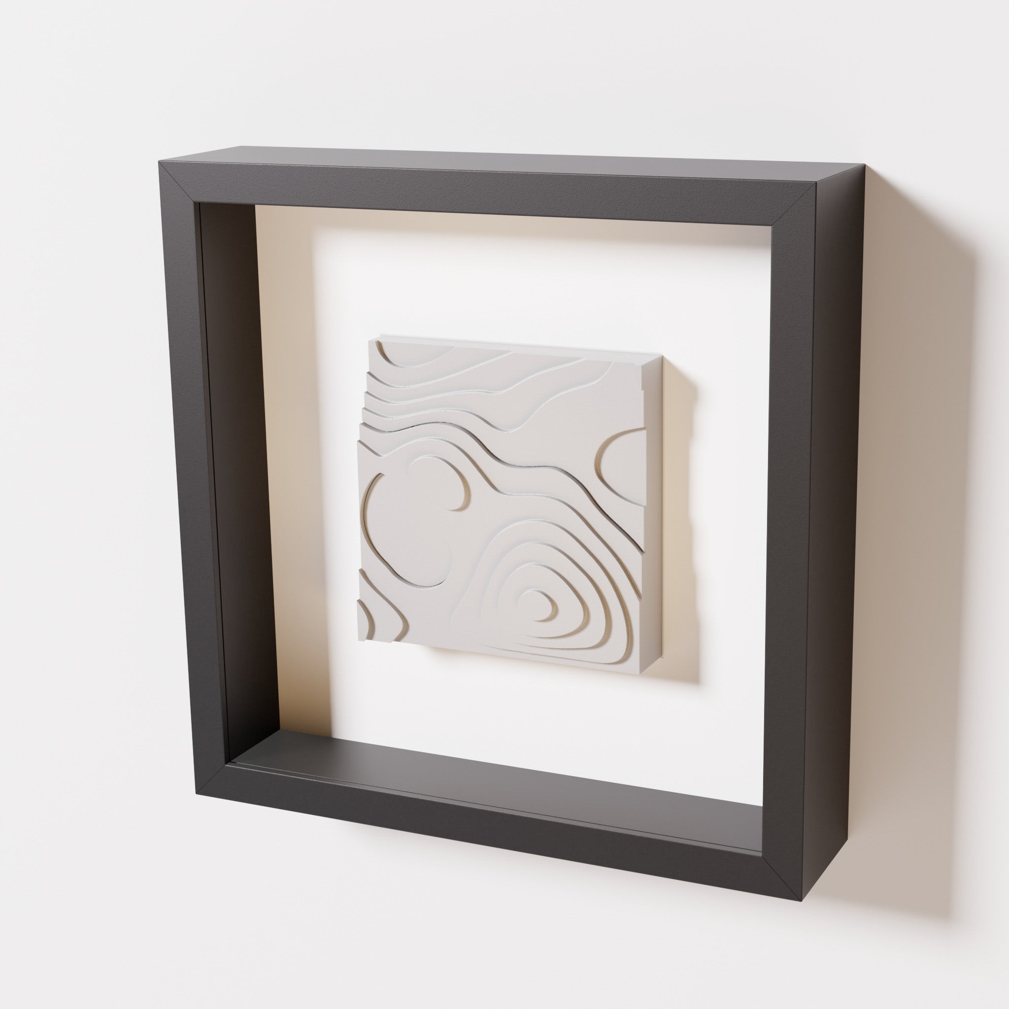 A close-up of a black shadowbox frame containing a marble white artwork depicting layered contour lines inspired by geographic elevation levels, showcasing intricate and geometric details.