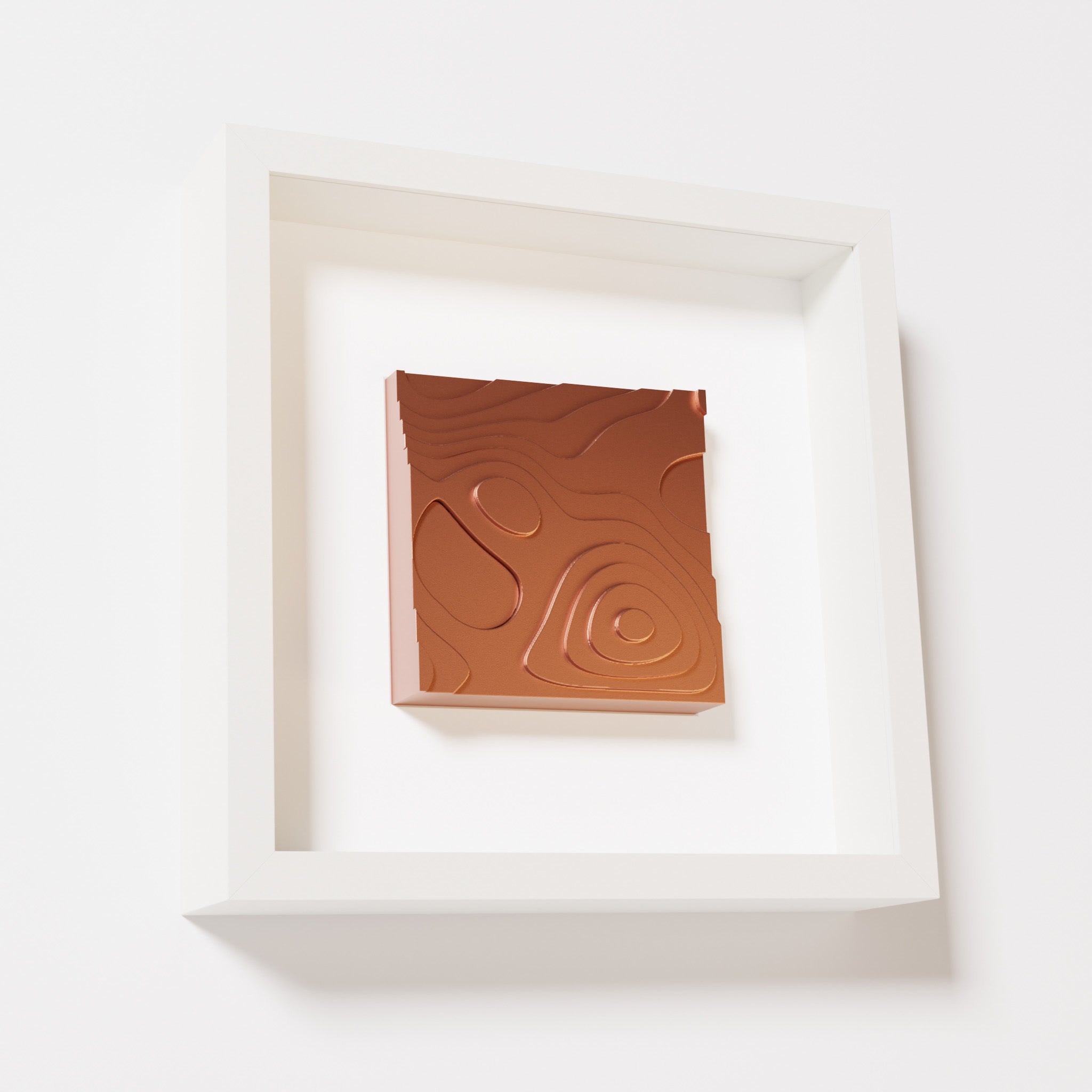 A close-up of a white shadowbox frame containing a chrome copper artwork depicting layered contour lines inspired by geographic elevation levels, showcasing reflective copper details.