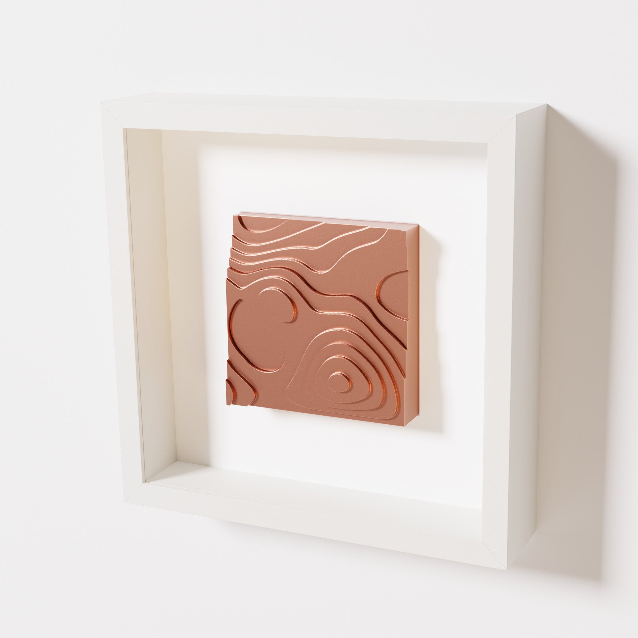 A close-up of a white shadowbox frame containing a chrome copper artwork depicting layered contour lines inspired by geographic elevation levels, showcasing reflective copper details.