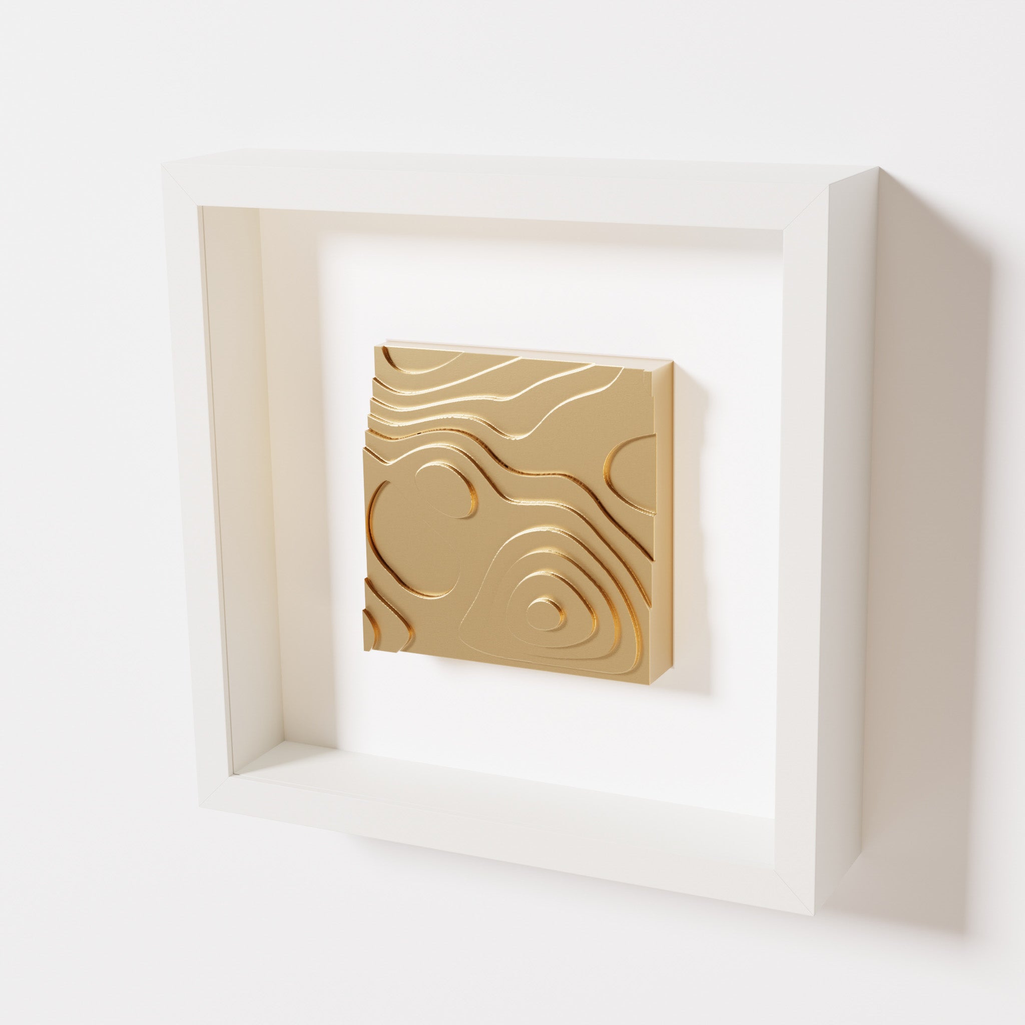 A close-up of a white shadowbox frame containing a chrome gold artwork depicting layered contour lines inspired by geographic elevation levels, showcasing reflective golden details.