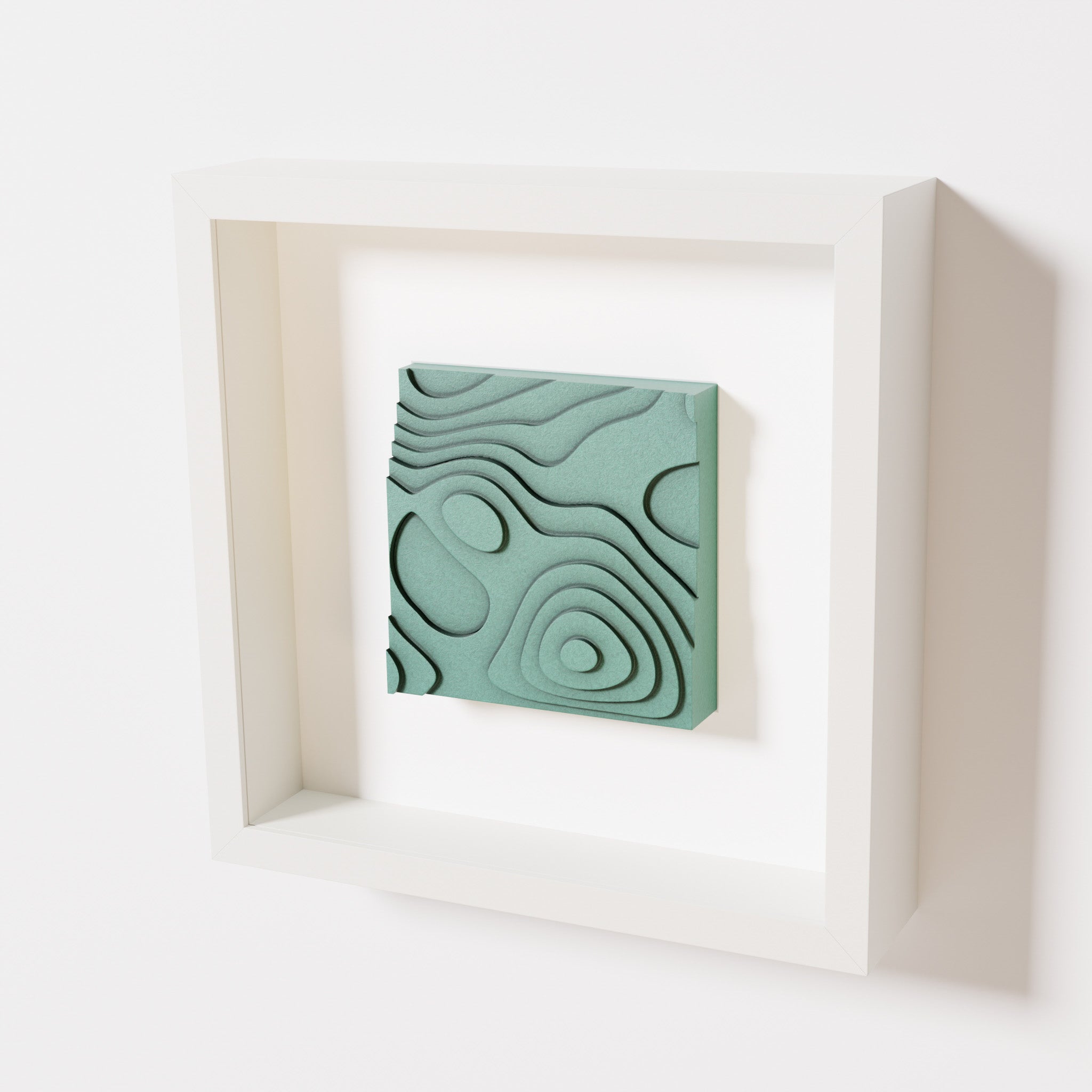 A close-up of a white shadowbox frame containing an old patina artwork depicting layered contour lines inspired by geographic elevation levels, showcasing intricate and geometric details with a textured green finish.