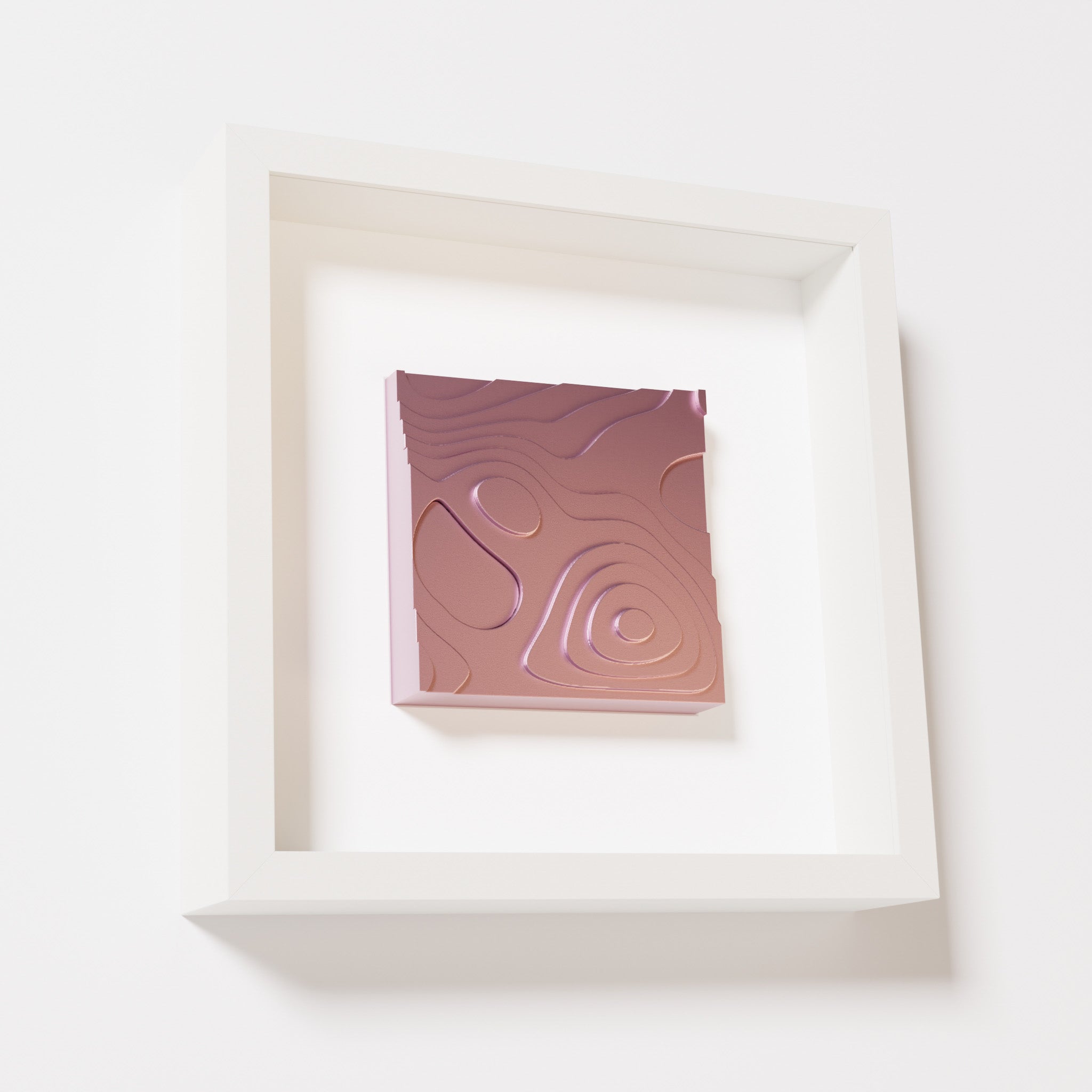 A close-up of a white shadowbox frame containing a metallic rose artwork depicting layered contour lines inspired by geographic elevation levels, showcasing reflective pink details.